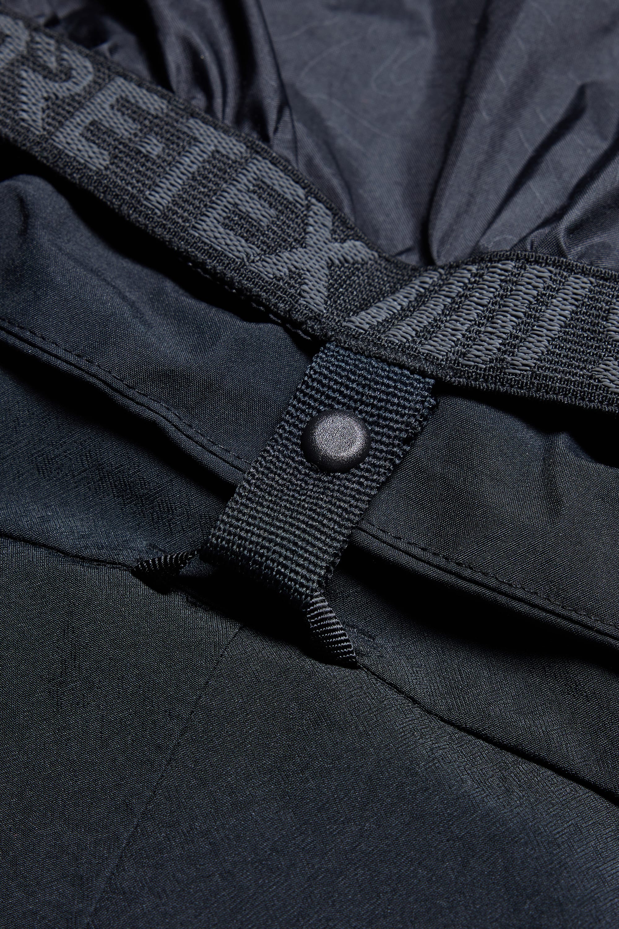 Close-up of a dark fabric jacket with a snap button and GORE-TEX waistband detail, highlighting texture and stitching. Pairs perfectly with the 686 Men's Deconstructed™ Denim Pant by 686 for all-weather protection.