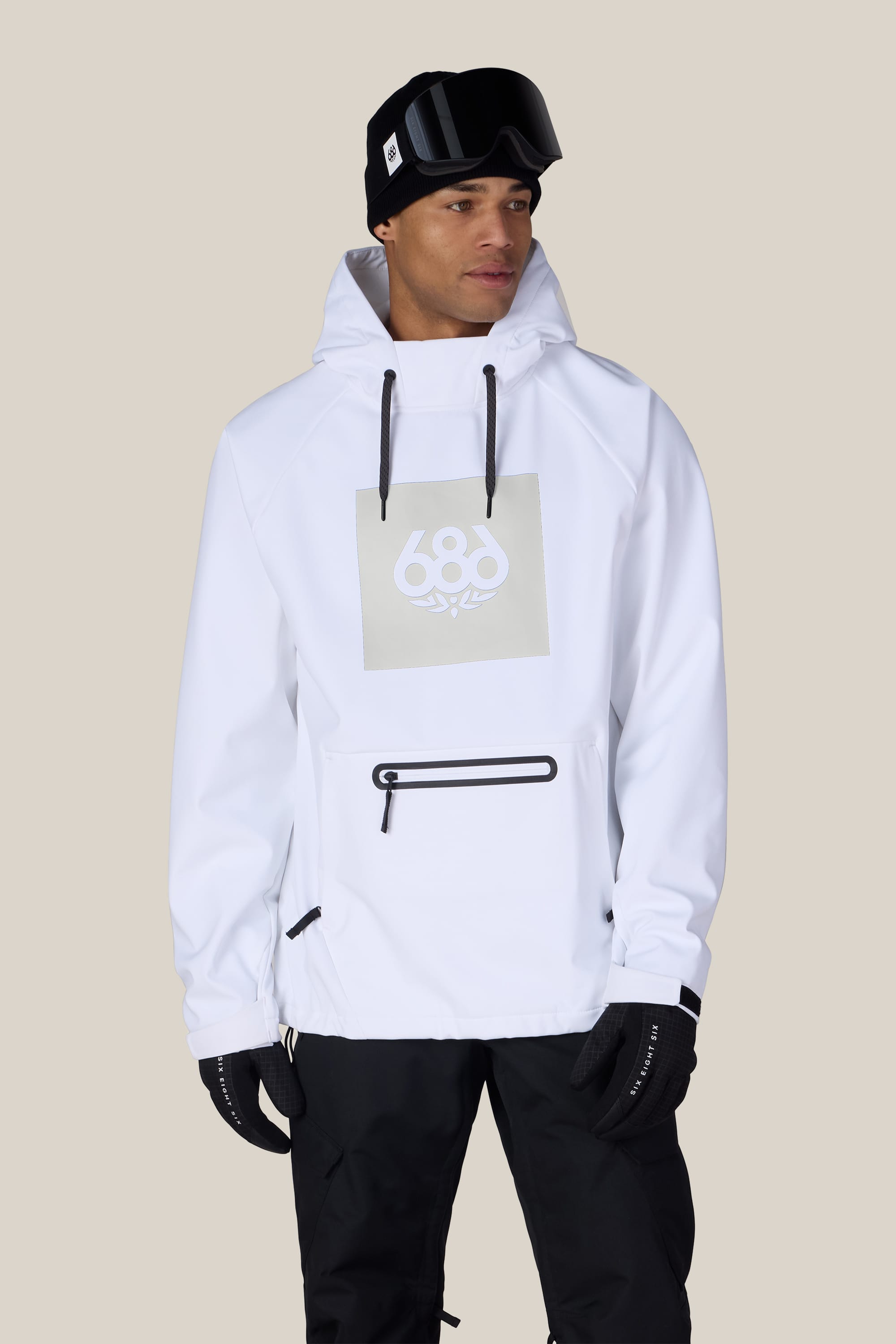 A man wearing the 686 Men’s Waterproof Hoody, featuring the 686 logo, along with black gloves, black pants, and a black beanie with goggles. He stands against a plain light background, looking slightly to his left.