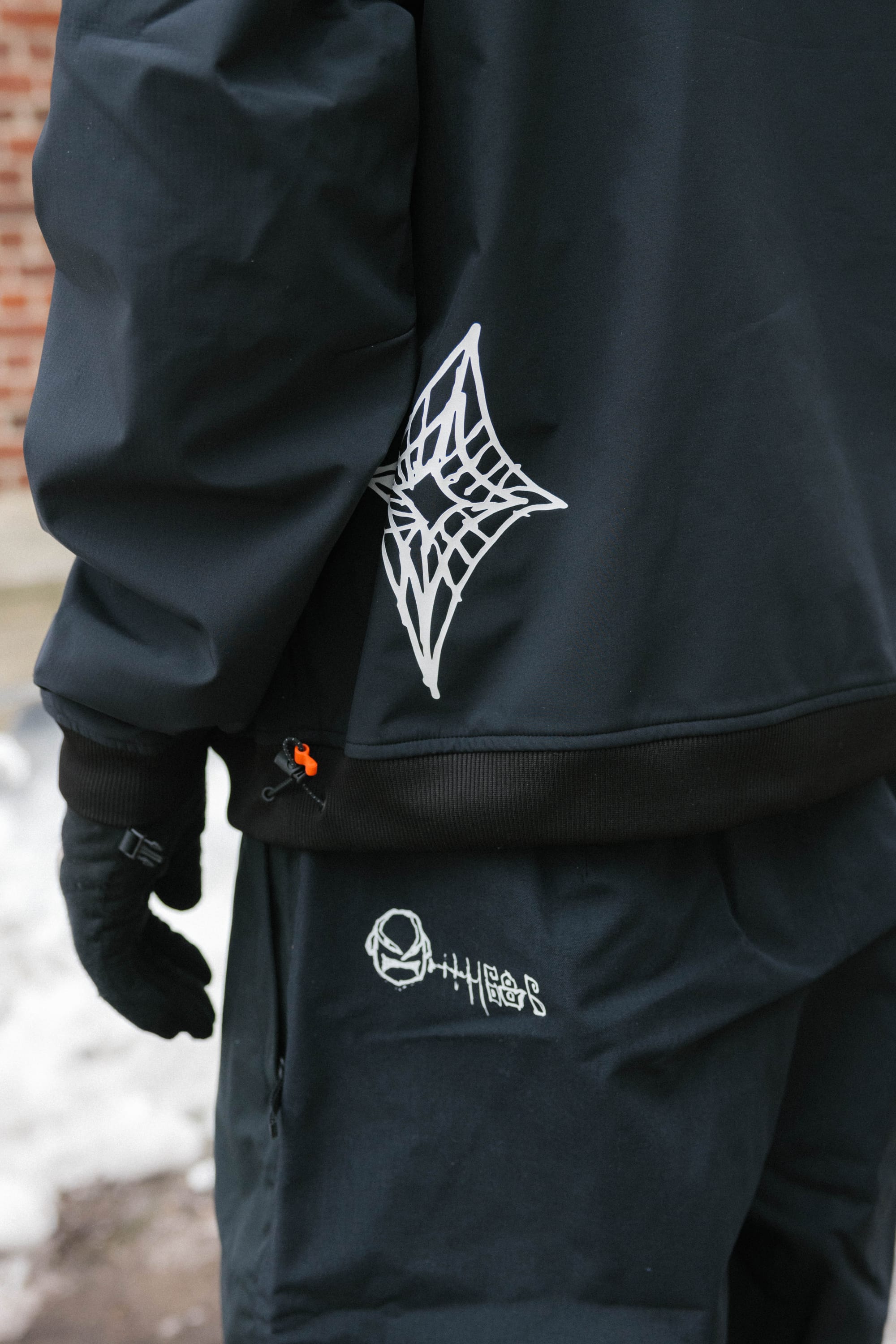 Wearing the 686 Mens Waterproof Team Hoody, a person stands outdoors in snowy weather. The black hoody with white graphics by 686 looks both warm and stylish, paired with gloves for a fashionable winter outfit.