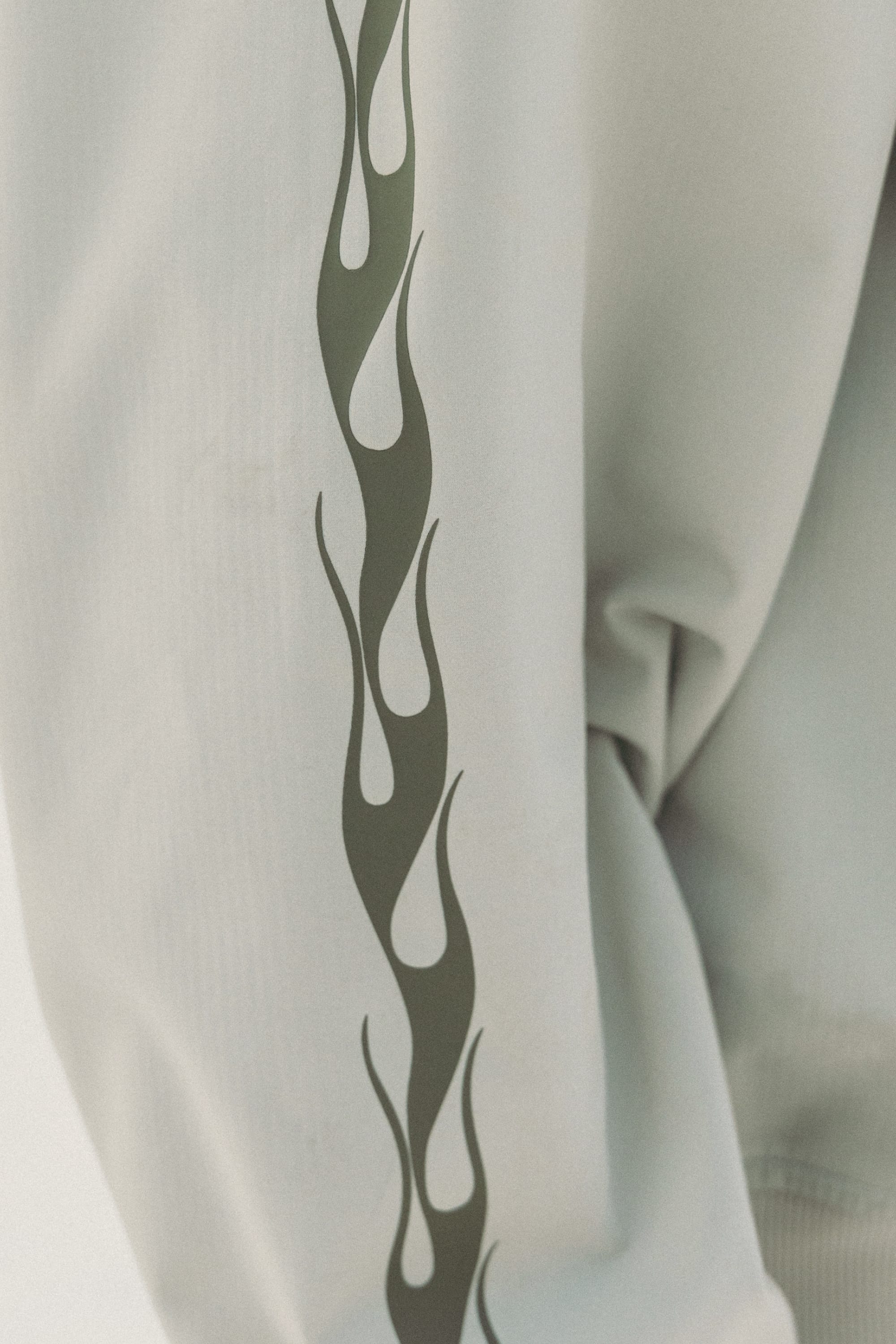 A close-up of the 686 Mens Waterproof Team Hoody sleeve in light grey, showcasing a vertical dark green flame design along the outer side.