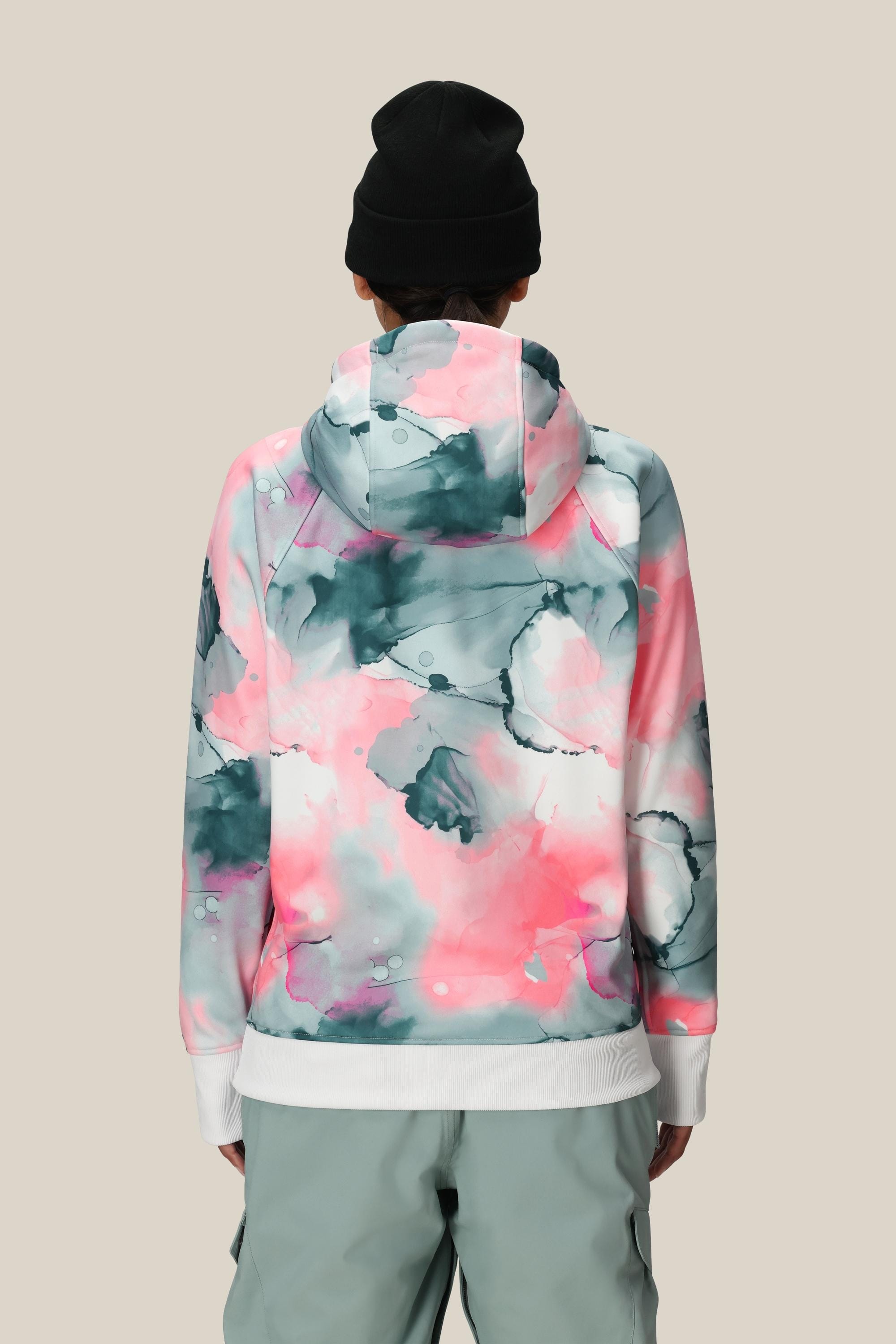 A person is seen from the back against a beige background, wearing a black beanie and the 686 Womens Bonded Fleece Pullover Hoody by 686 in a pink, white, and teal watercolor pattern with cozy fleece lining.