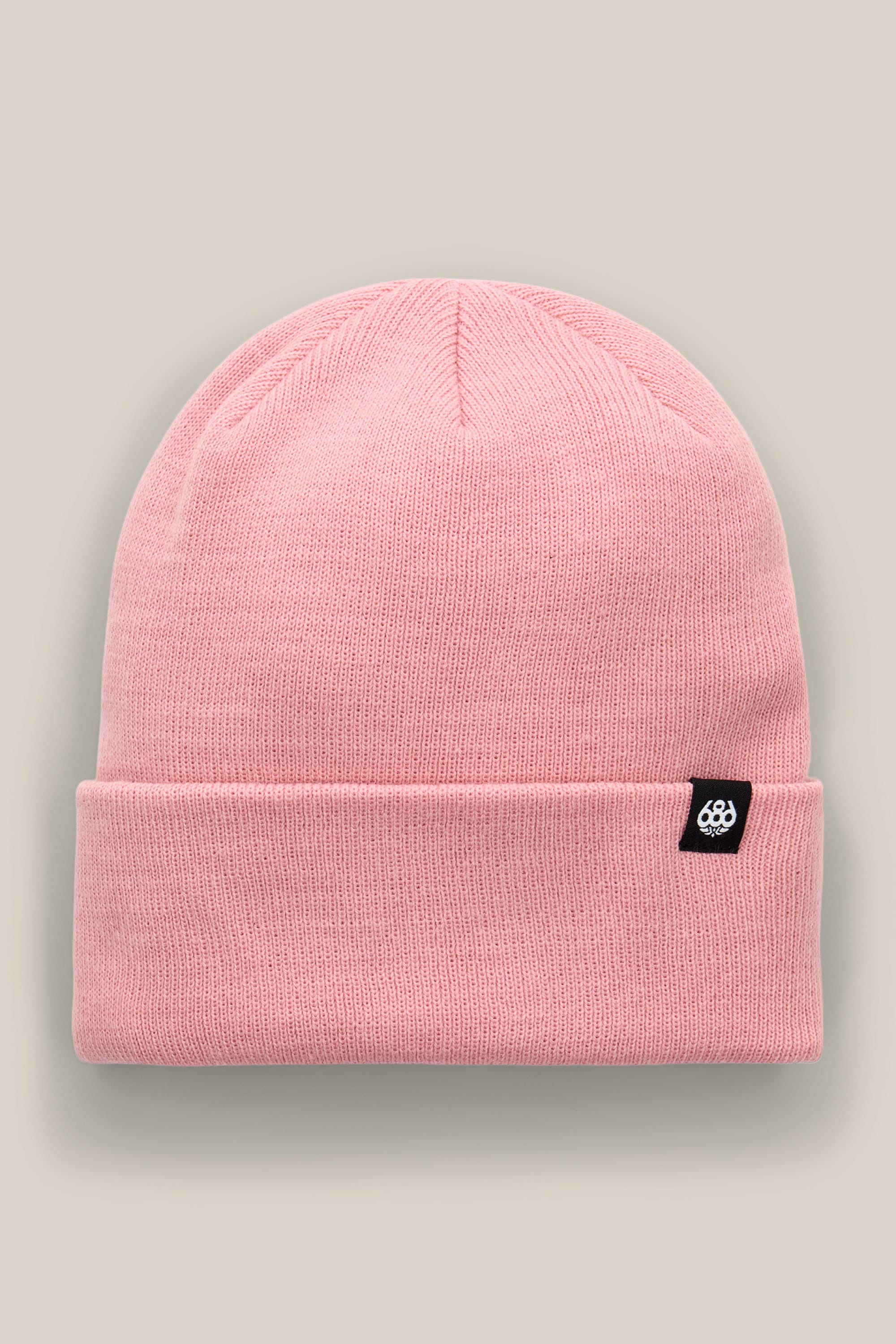 The 686 Standard Roll Up Beanie by 686 is a pink knit beanie featuring a folded brim and a small black tag with a white logo, shown against a neutral beige background.