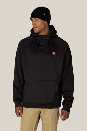 A person wearing a black beanie and the 686 Men’s Bonded Fleece Pullover Hoody by 686, paired with beige pants, stands against a light beige background, looking to the side.