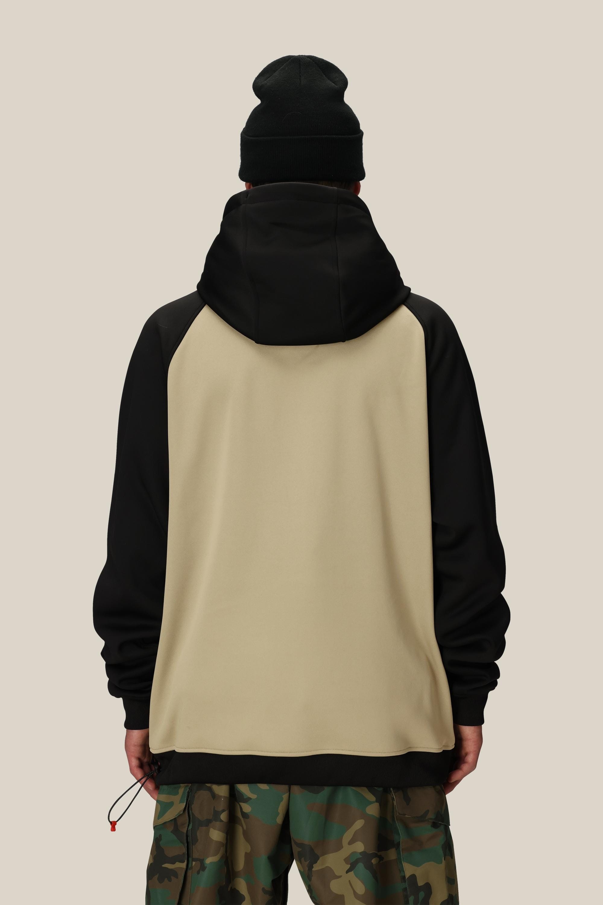 A person wearing the 686 Mens Bonded Fleece Pullover Hoody in beige and black, paired with a black beanie and camo pants, stands facing away from the camera against a plain light beige background.