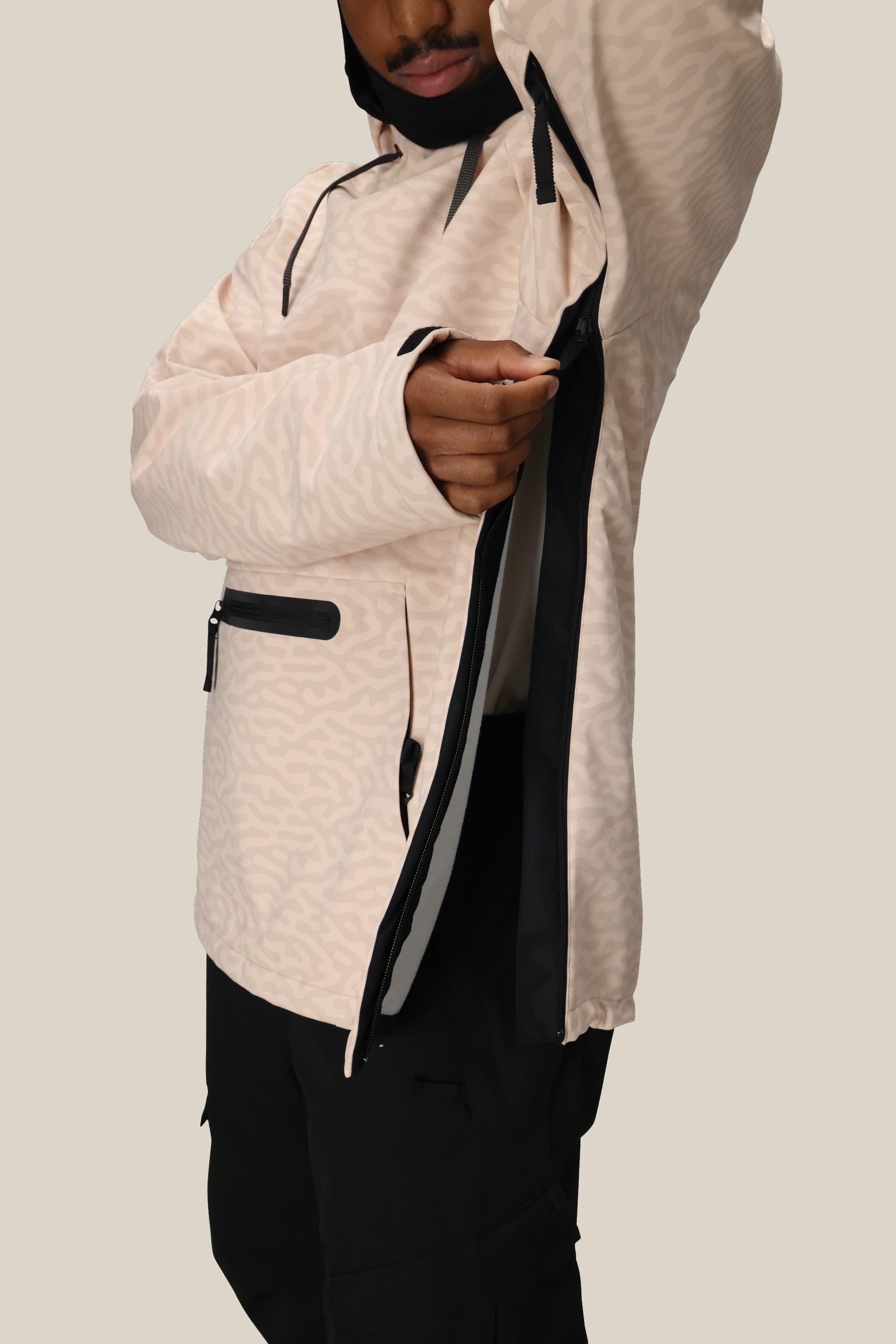 A person in the 686 Mens Waterproof Hyperchromic Pullover Hoody with 10k waterproofing and dark pants unzips a large side vent, revealing the interior secure pocket, against a plain light background.