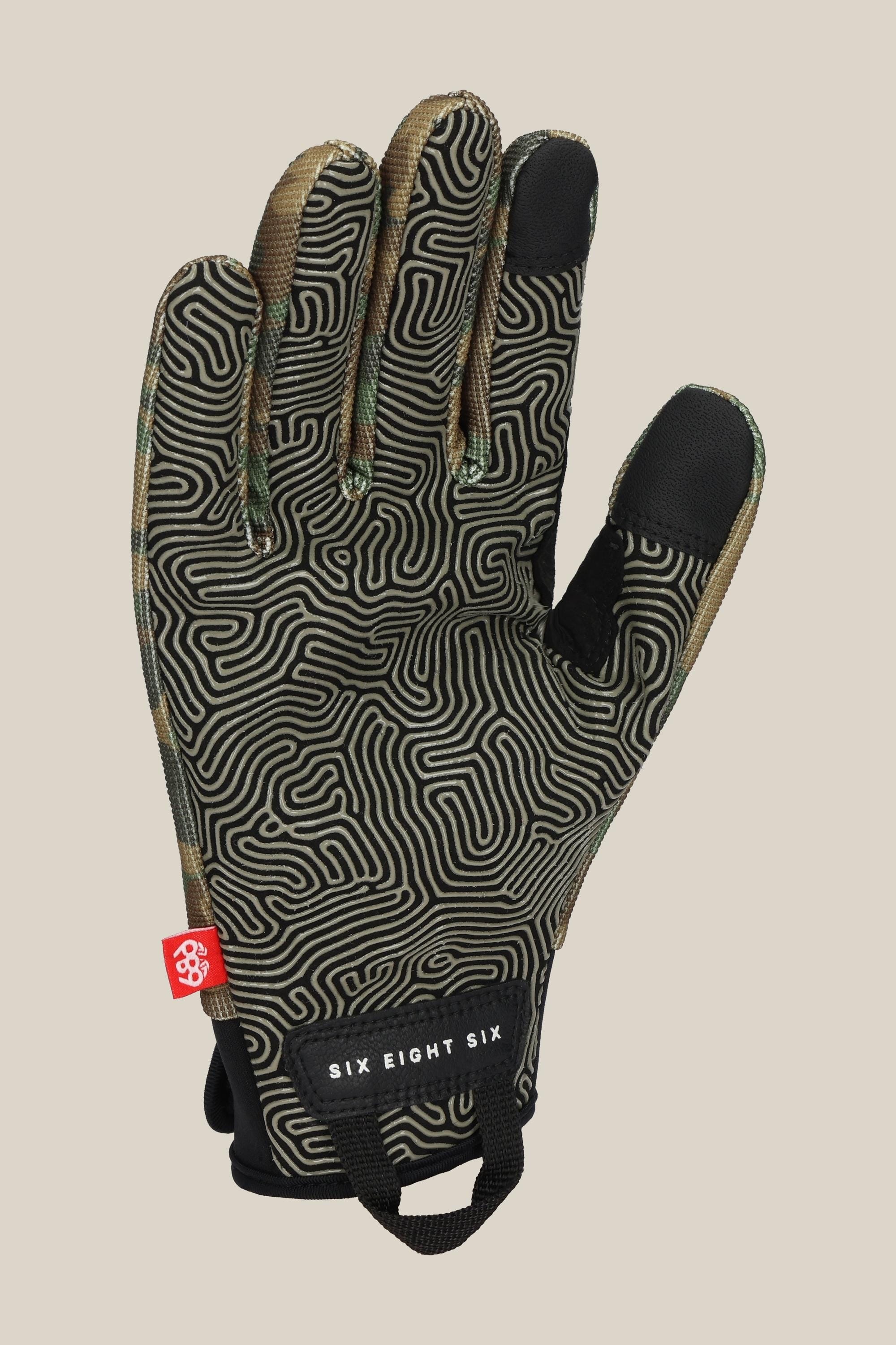 The 686 Outlaw Pipe Glove by 686 features a black design with a beige maze pattern, a small red tag, and a black wrist strap labeled "SIX EIGHT SIX" in white, shown on a plain beige background.
