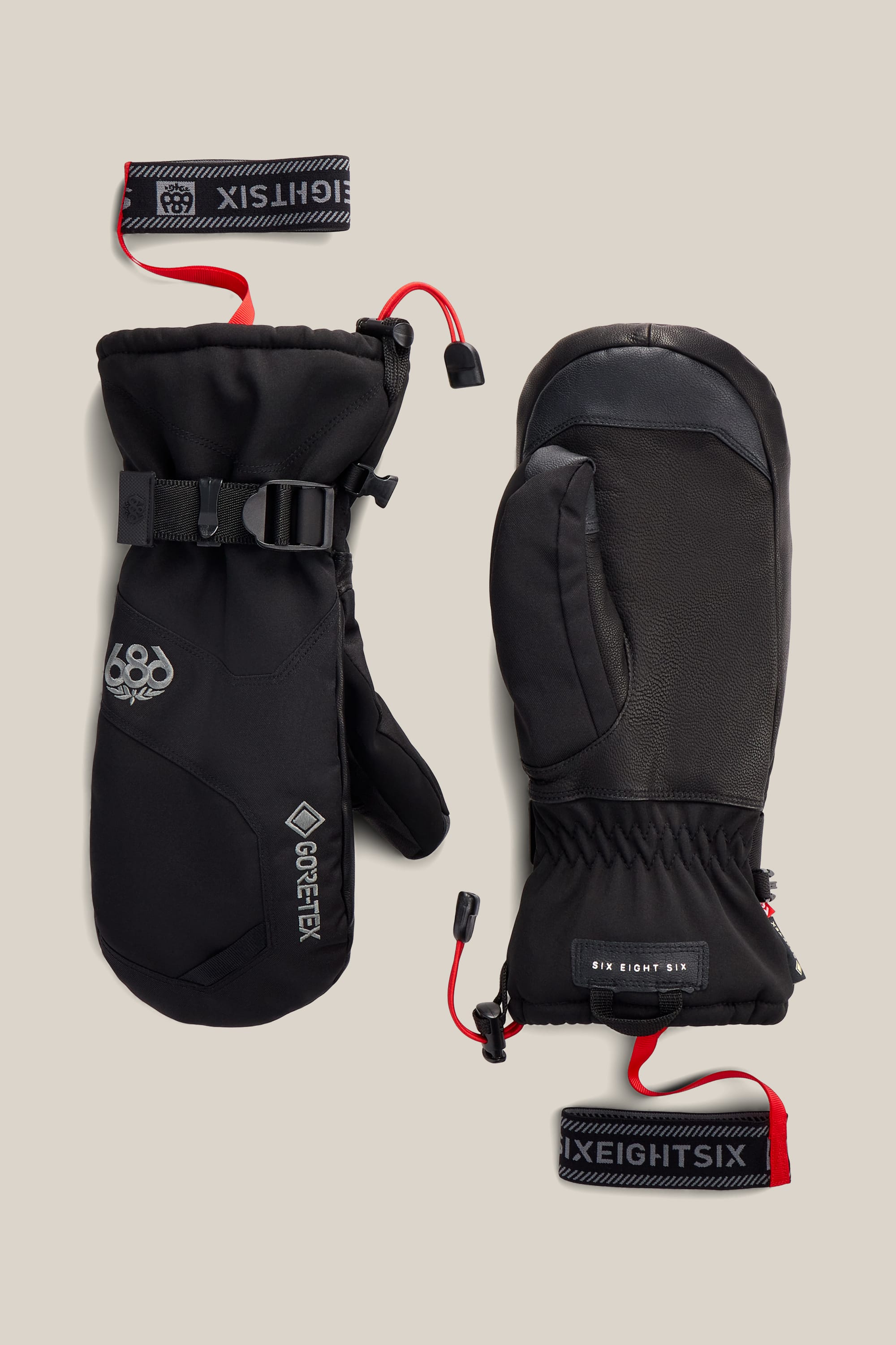 A pair of 686 Men’s GORE-TEX® Leather Linear™ Mitts in black, featuring red wrist straps, adjustable buckles, and visible 686 branding. One mitten displays the 686 logo and a GORE-TEX label, while the other features additional branding and textured palm detailing.