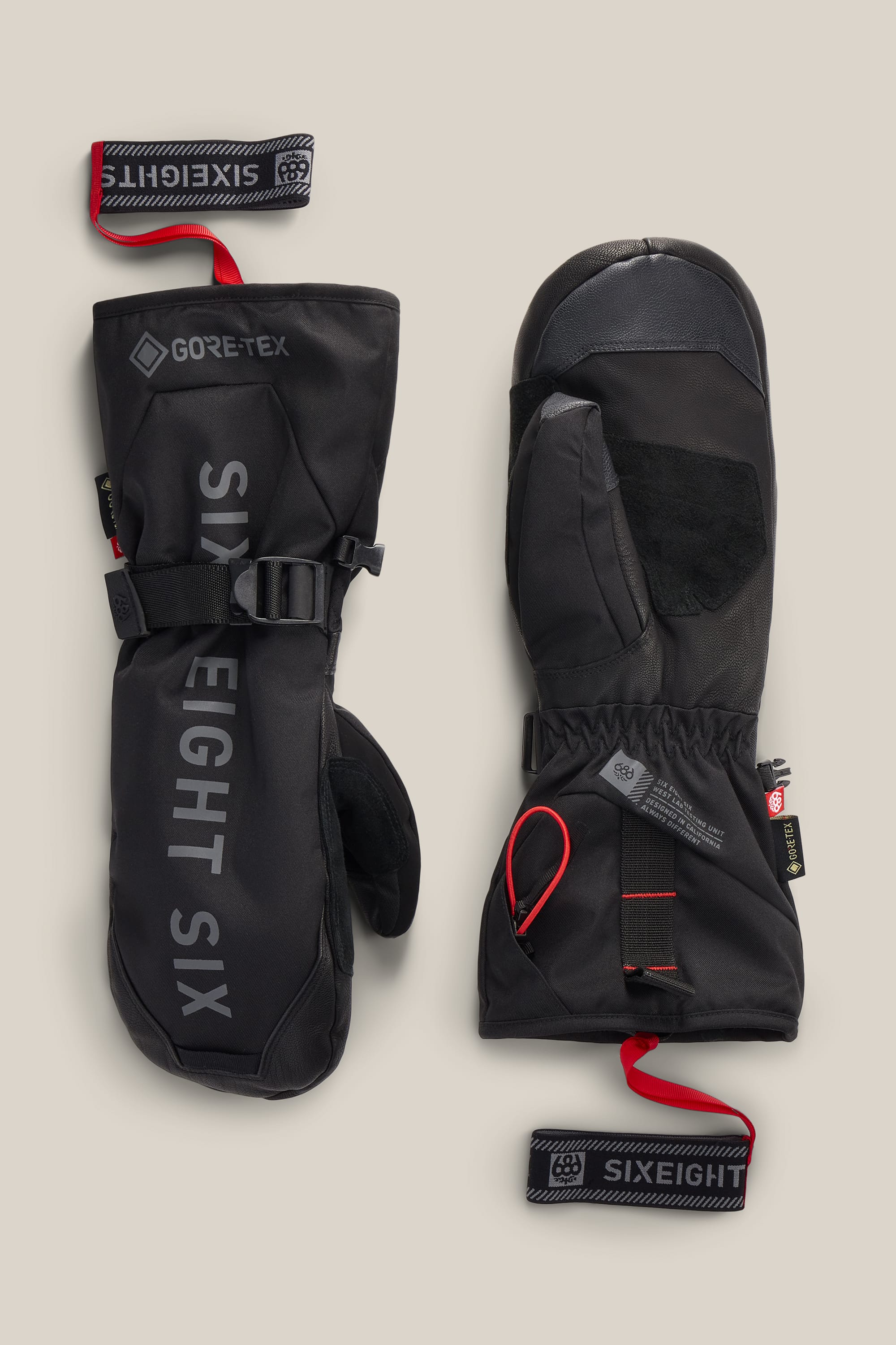 A pair of 686 Men’s GORE-TEX® Leather Deep Days™ Mitts in black, featuring the 686 branding on one mitt. The design includes red pull loops, wrist straps, and a leather palm grip, all presented against a neutral background.