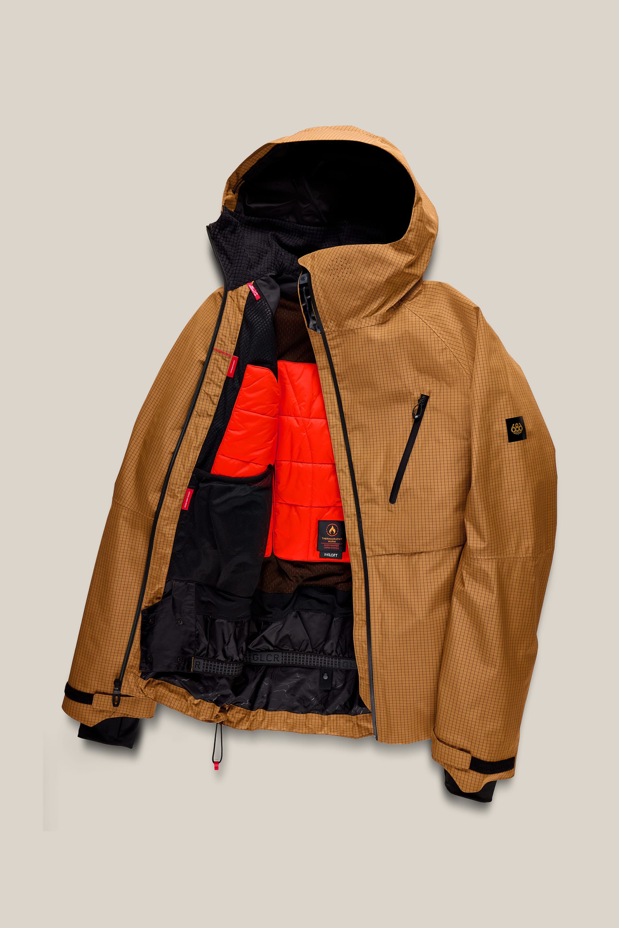 The 686 Men’s Hydra™ Thermagraph® Jacket by 686, featuring a brown hood and grid pattern, is displayed unzipped to showcase its vibrant orange quilted inner lining and multiple black pockets, set against a plain beige background.