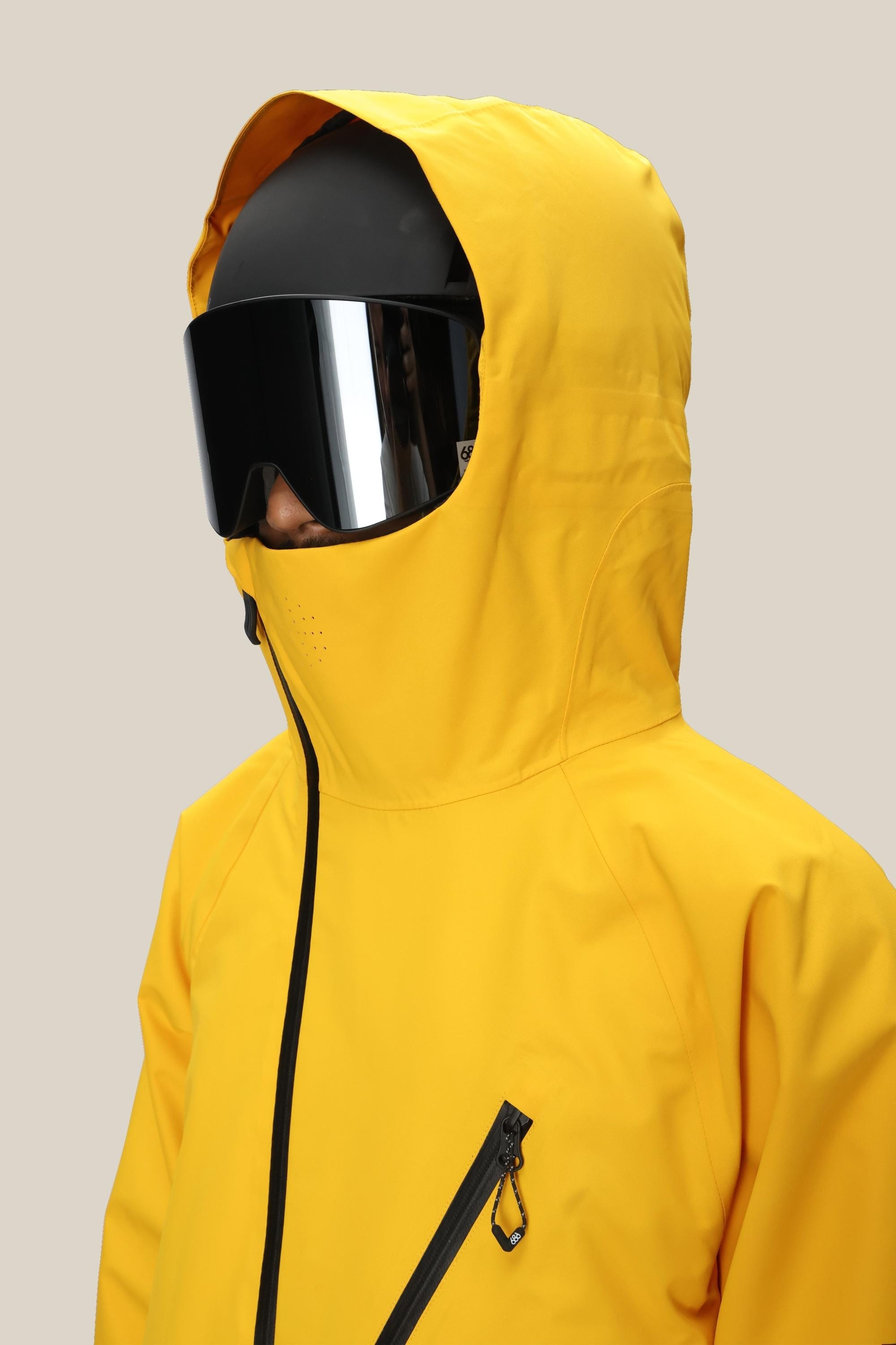 A man wears the 686 Men’s Hydra™ Thermagraph® Jacket in bright yellow, featuring a visible zipper and chest loop, paired with oversized black ski goggles and a black helmet, facing left against a plain light background.