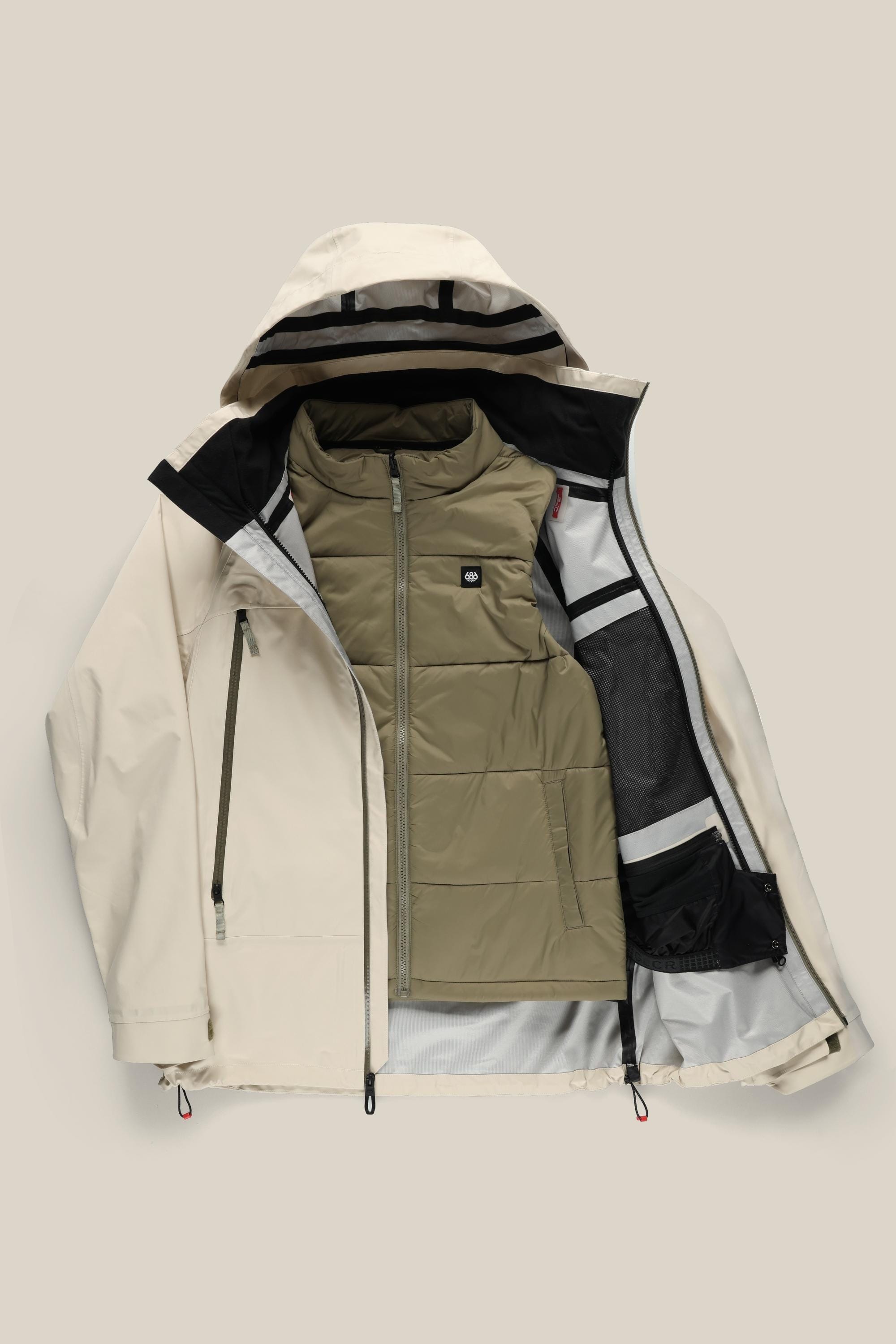 The 686 Men’s SMARTY® 3-In-1 Rodeo™ 3L Jacket by 686 is shown unzipped to display its olive green, quilted inner vest. This beige jacket features black zipper accents and mesh inner pockets, and is laid flat against a neutral background.