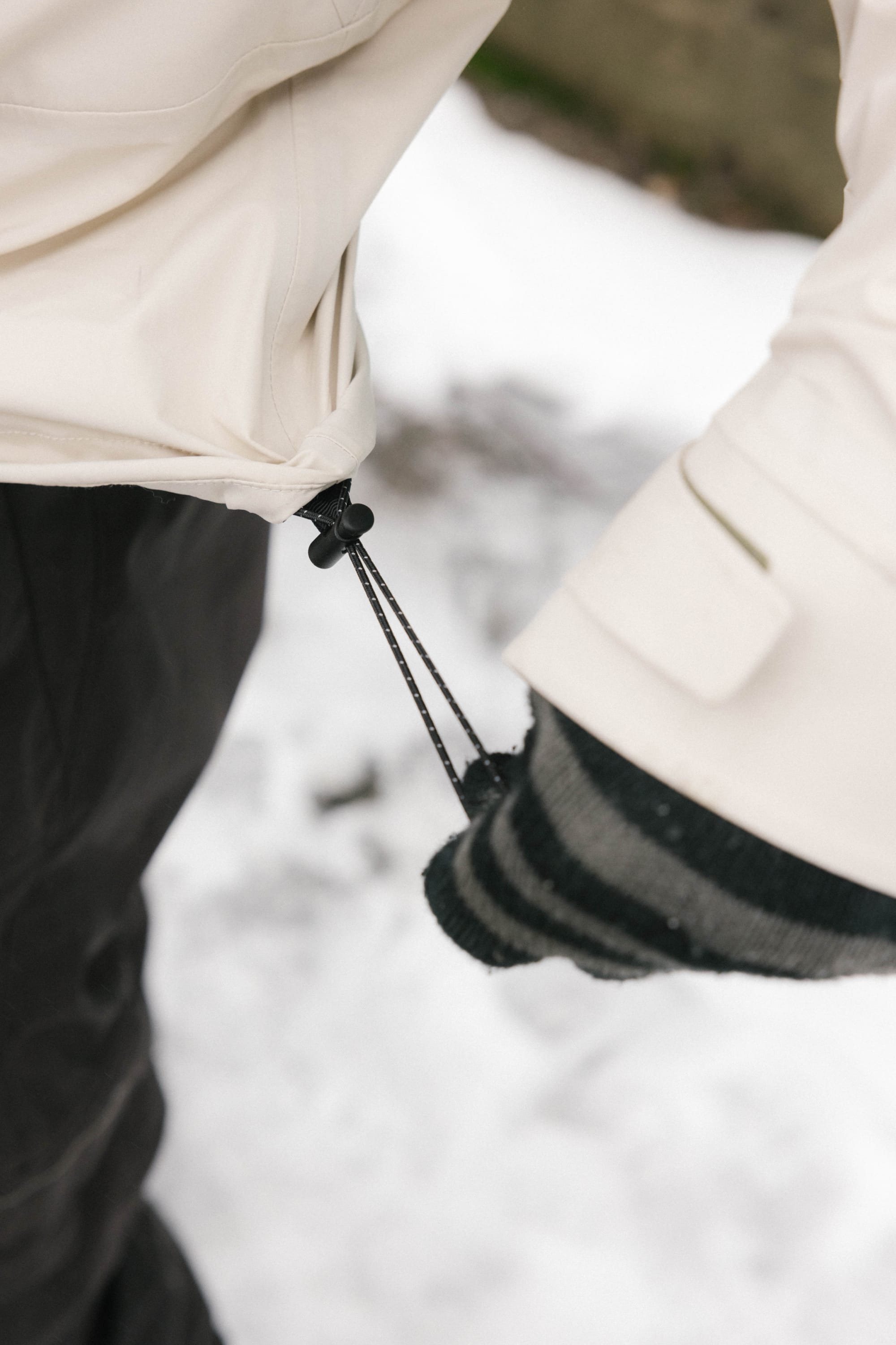 A person wearing the 686 Men's SMARTY® 3-In-1 Rodeo™ 3L Jacket adjusts its hem drawstring while standing on snow, paired with striped gloves.
