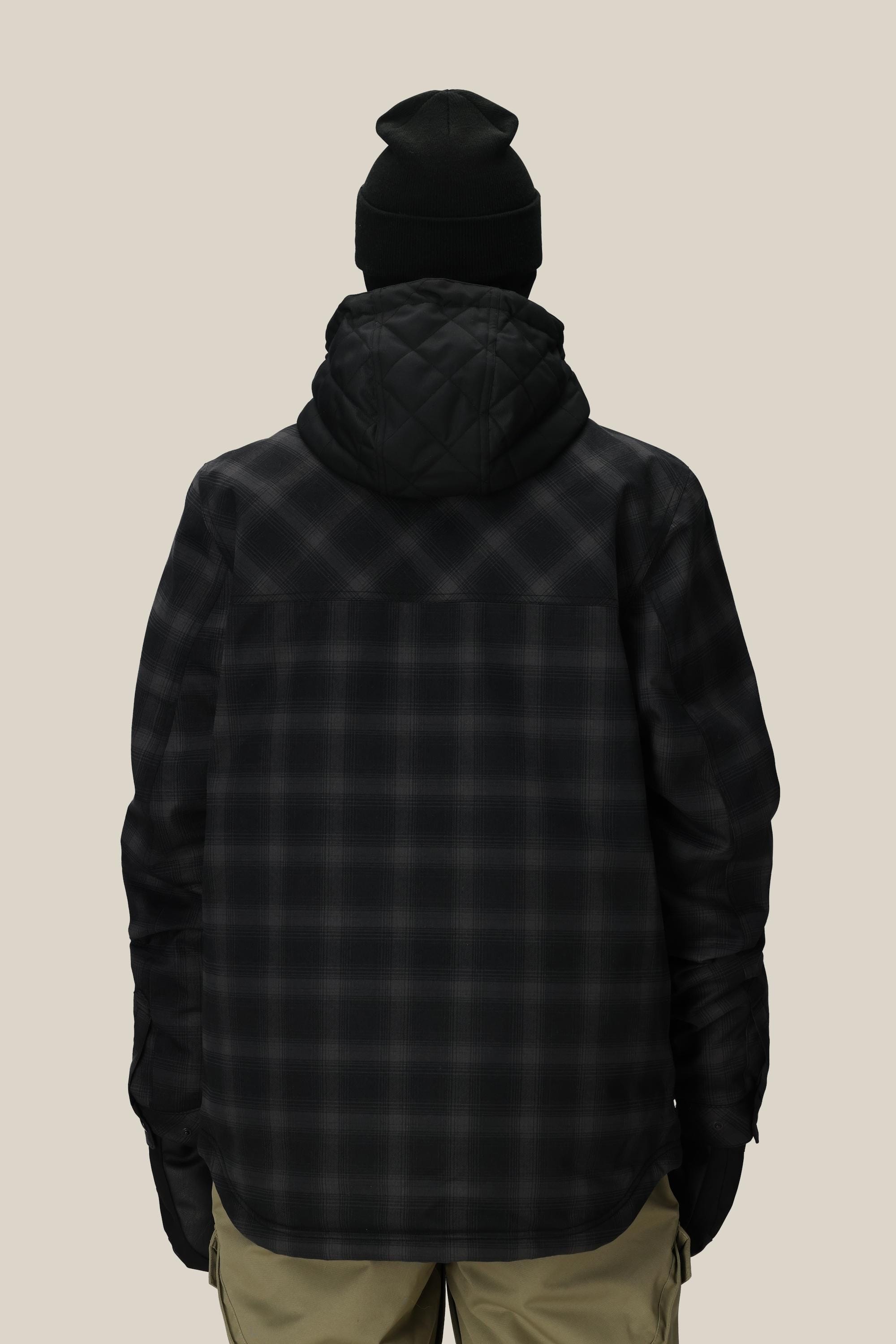 A person is shown from the back against a plain light background wearing a black beanie, khaki pants, and the 686 Men's Woodland™ Insulated Jacket by 686 in dark plaid.