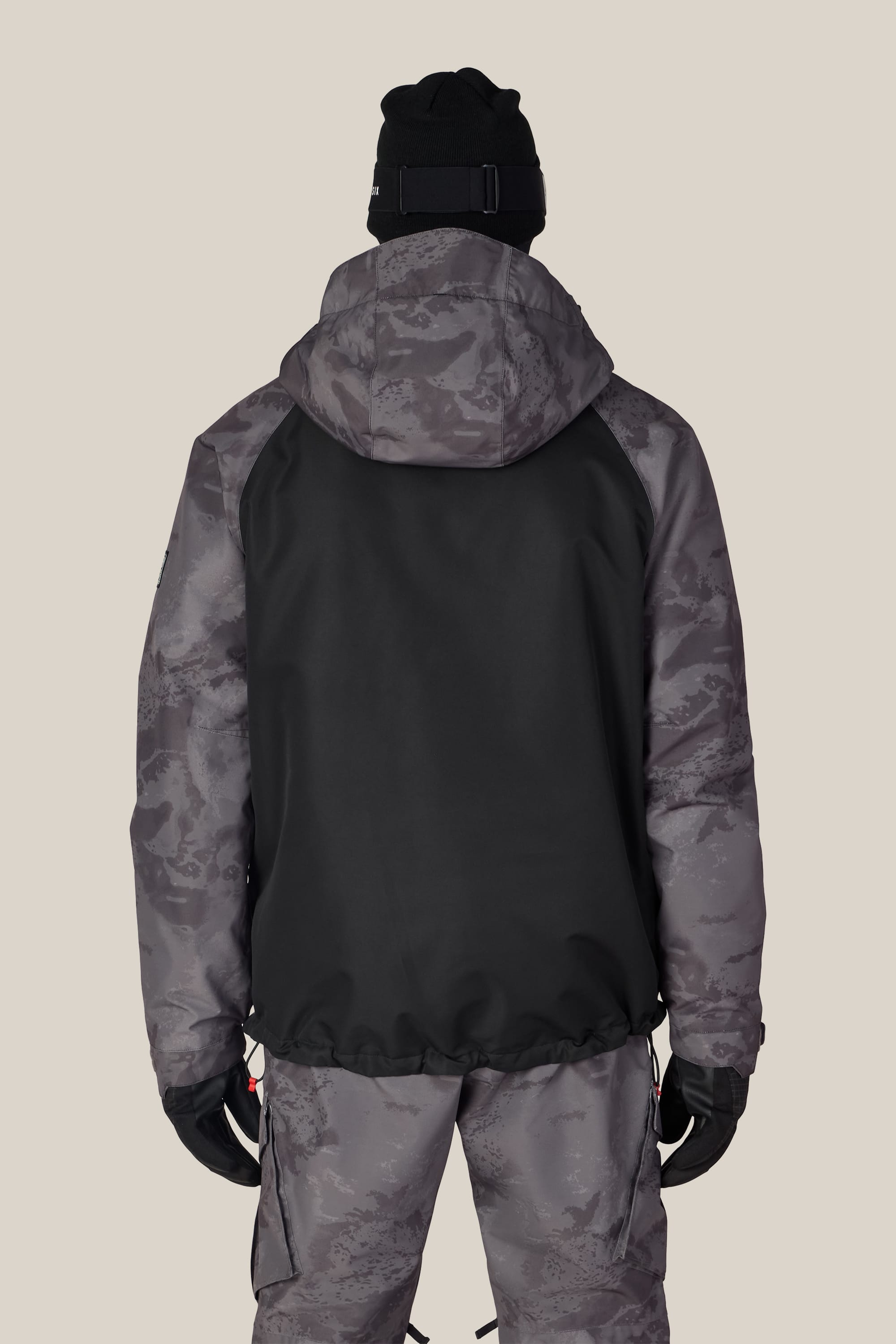 A person wearing the 686 Men’s Geo™ Insulated Jacket by 686 in a black and gray camo pattern, along with matching camo pants, black gloves, and a black beanie, stands facing away from the camera against a plain background.