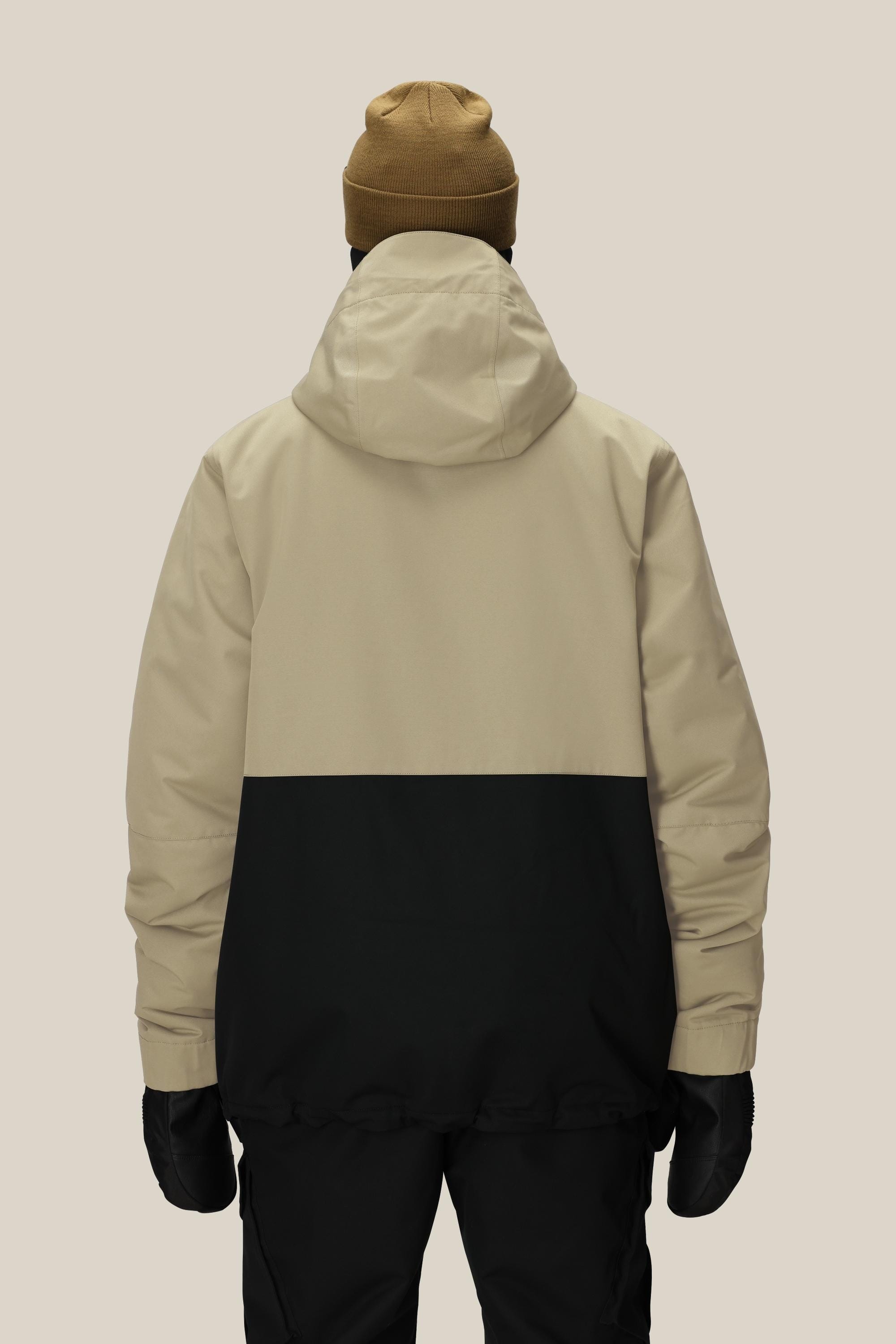 A person wearing a tan and black 686 Men's Foundation™ Insulated Jacket, black pants, black gloves, and a brown beanie stands facing away against a plain light background.