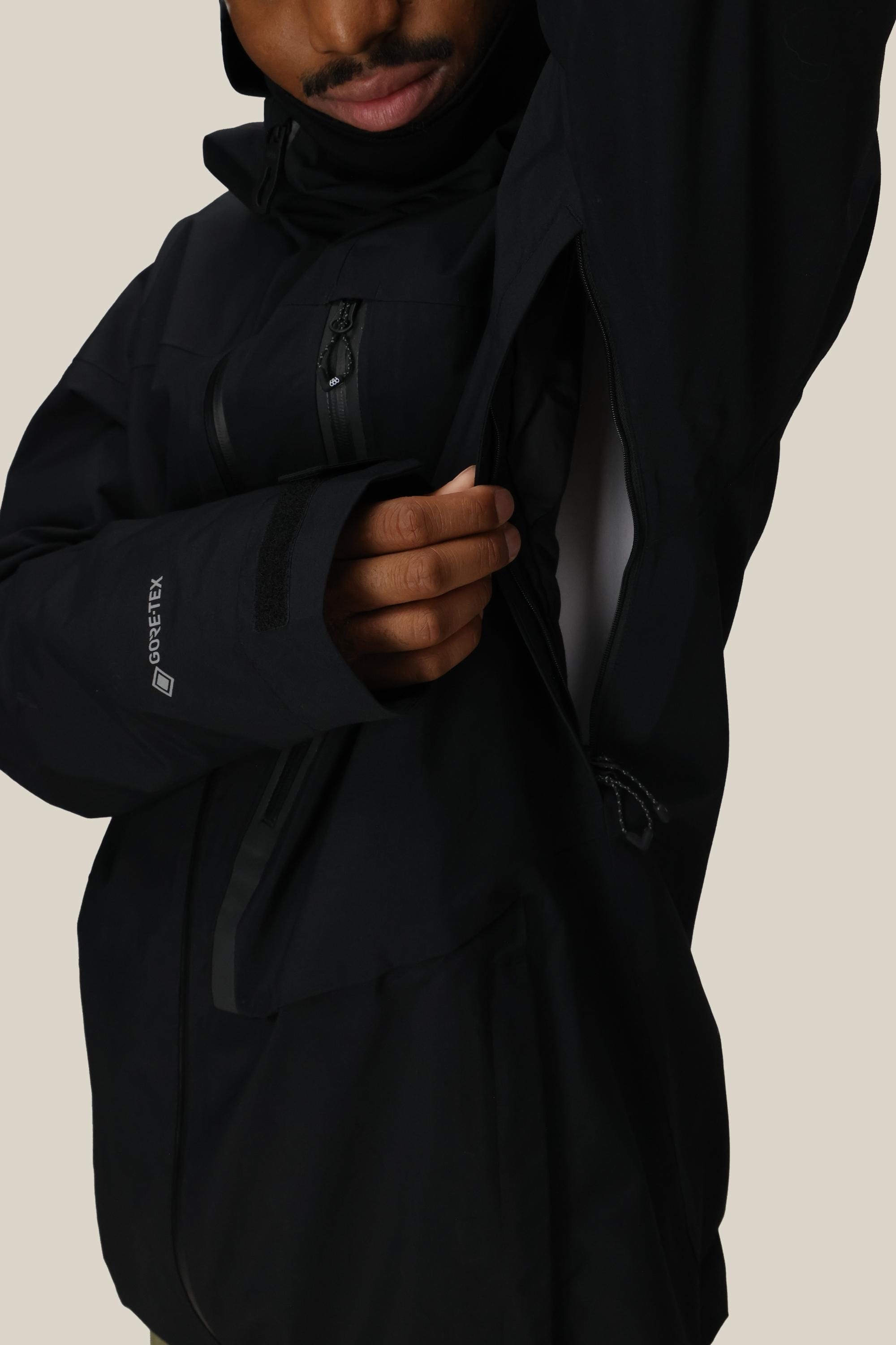 A person unzipping the ventilation opening of the black 686 Men’s GORE-TEX® GT Thermagraph® Jacket, with part of their face and hand visible against a plain background.