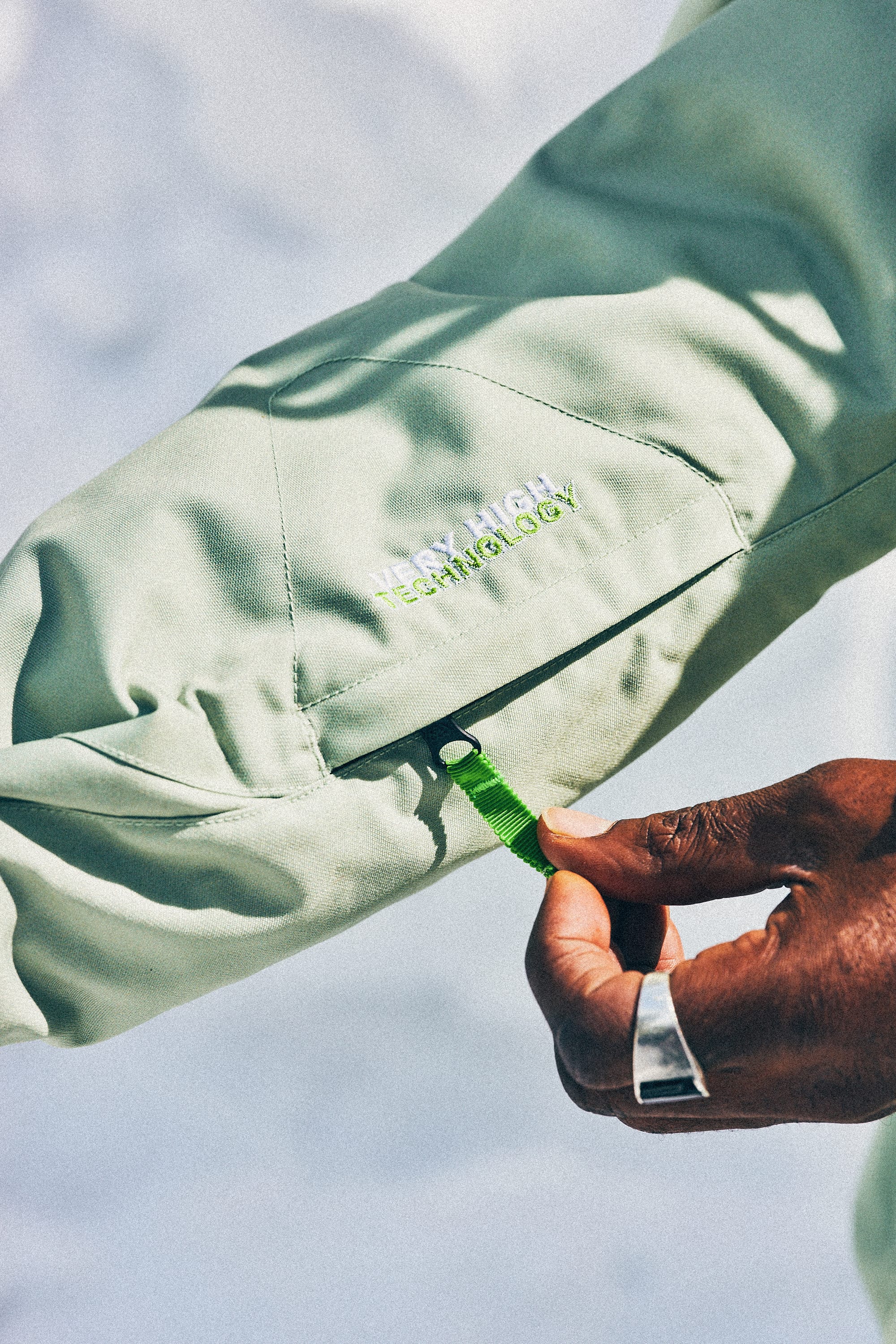 A close-up of a person’s hand adjusting a green strap on the sleeve of the 686 Mens HUF Double H Shell Jacket, a waterproof jacket by 686 featuring white embroidered text reading VENTING TECHNOLOGY.