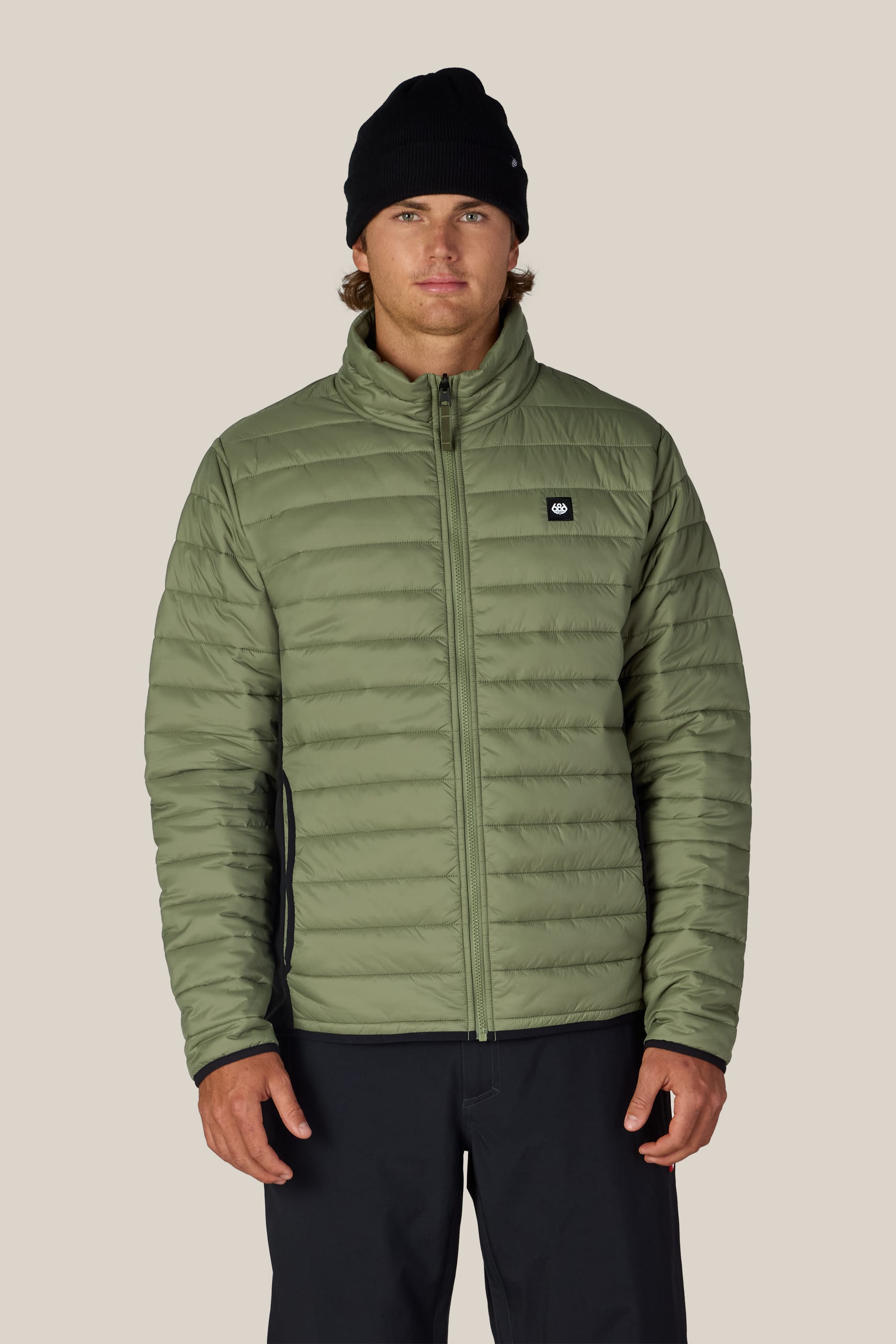A person wearing the 686 Men’s SMARTY® 3-In-1 Form Jacket in light green, along with black pants and a black beanie, stands facing forward against a plain light background.