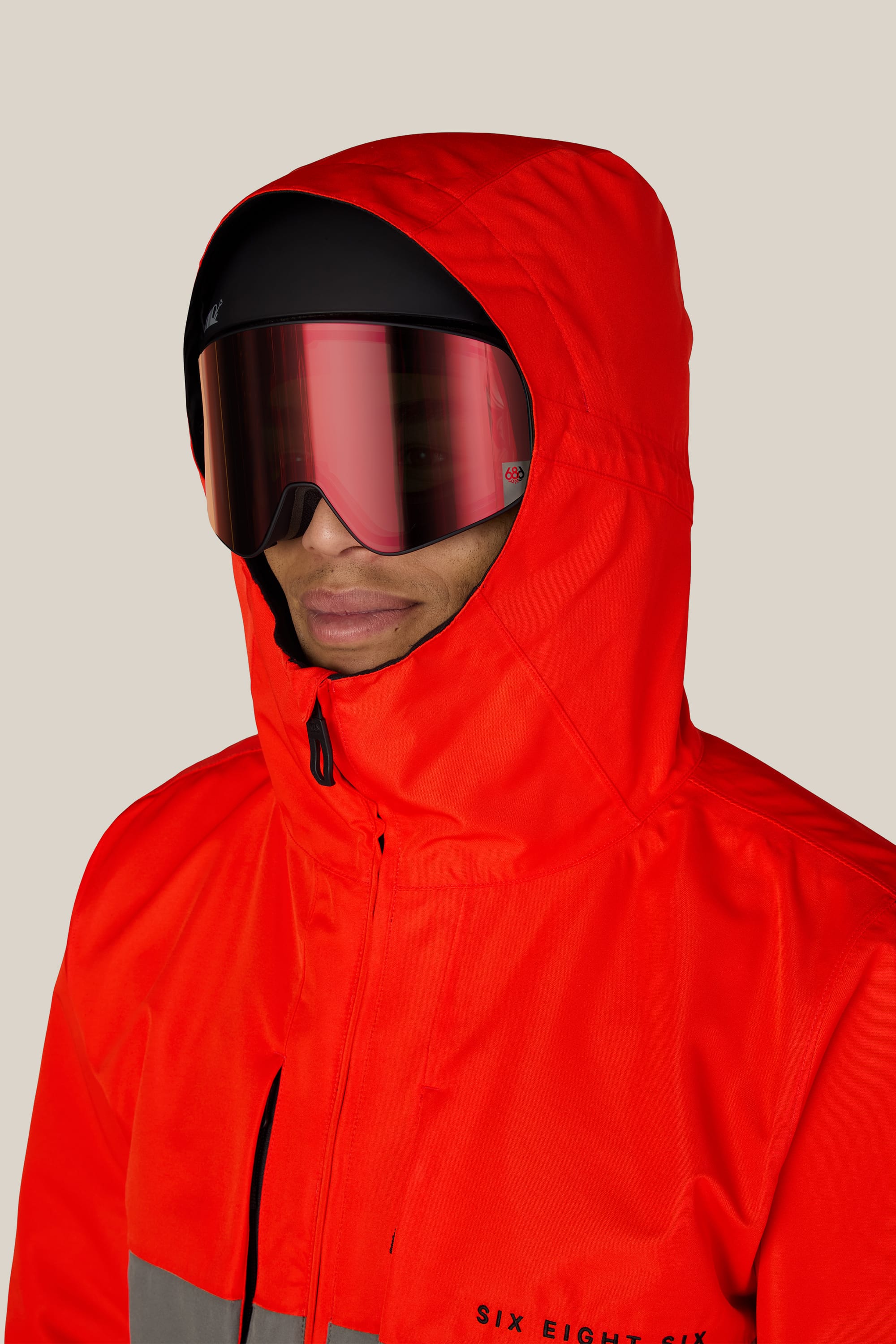 A man wearing the 686 Men’s SMARTY® 3-In-1 Form Jacket in bright red and large reflective ski goggles, facing slightly to the left against a plain beige background.