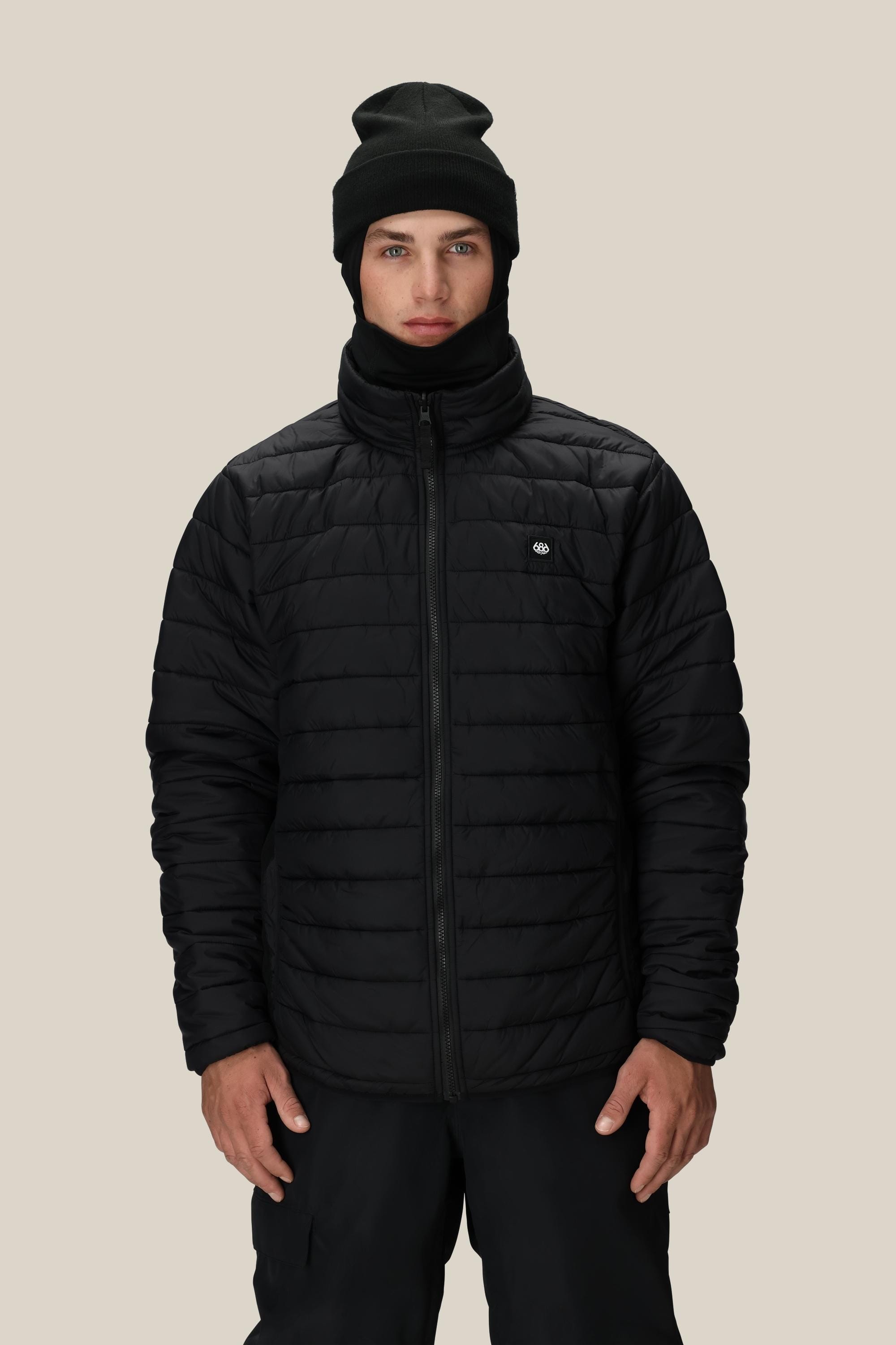 A person wears the 686 Men's SMARTY® 3-In-1 Form Jacket, paired with a black beanie and black pants, standing against a plain beige background and facing forward with a neutral expression.