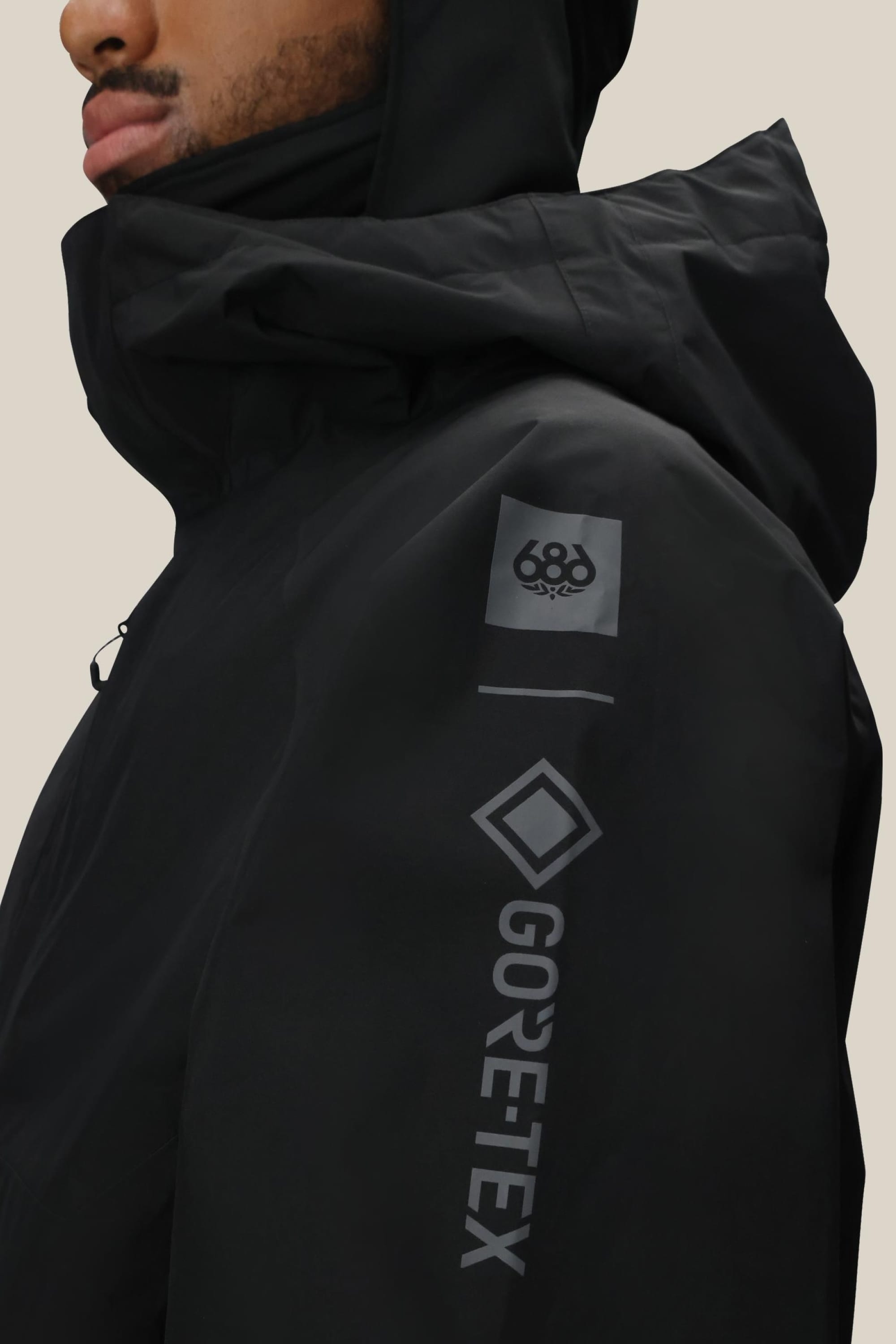 A man is seen in profile wearing the 686 Mens GORE-TEX Core Shell Jacket in black, featuring gray “GORE-TEX” and “686” logos on the sleeve, set against a plain background.