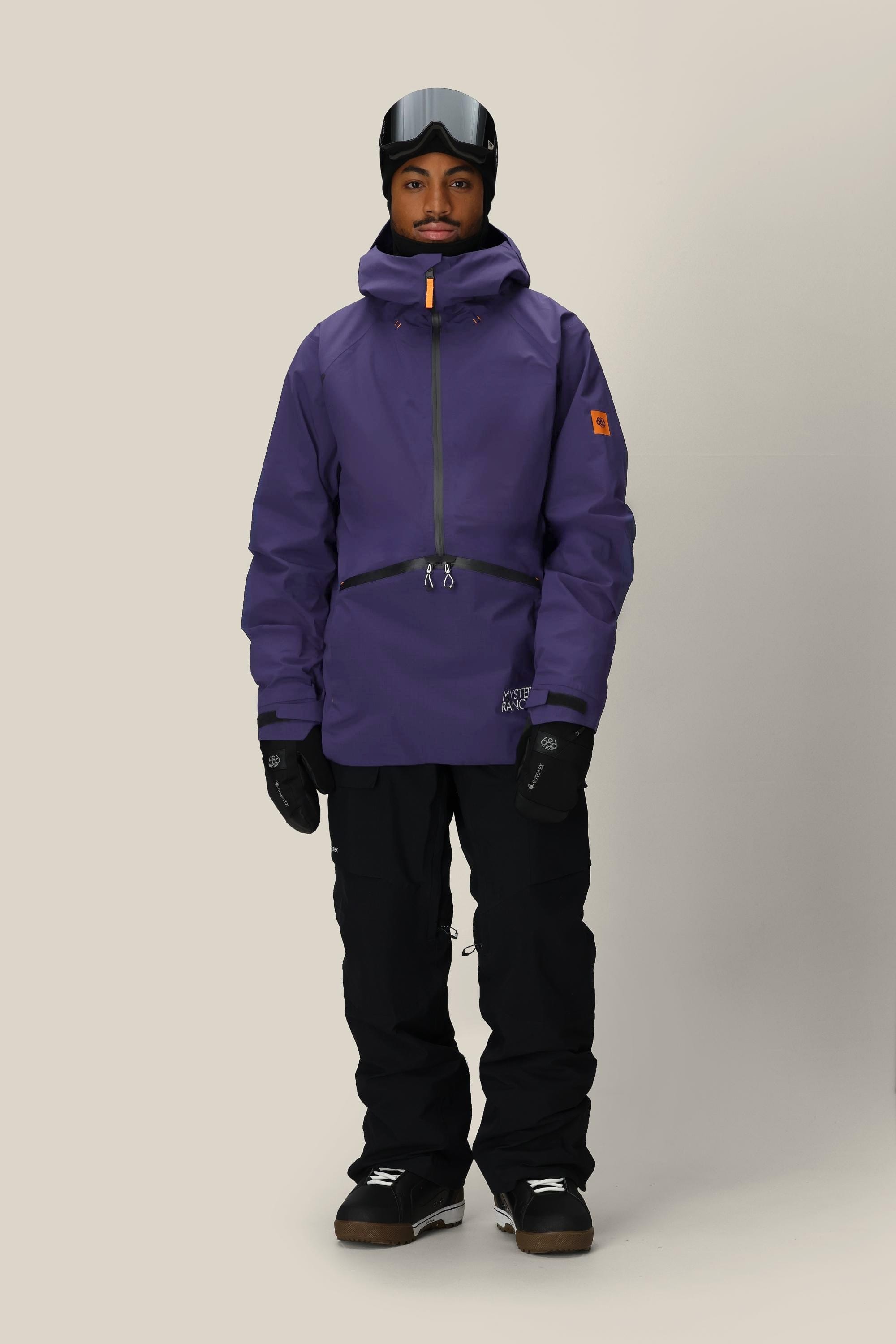 A person wearing the 686 Men's Mystery Ranch Qi 3L Shell Jacket in purple, along with black snow pants, gloves, boots, a helmet, and goggles stands against a plain light background.