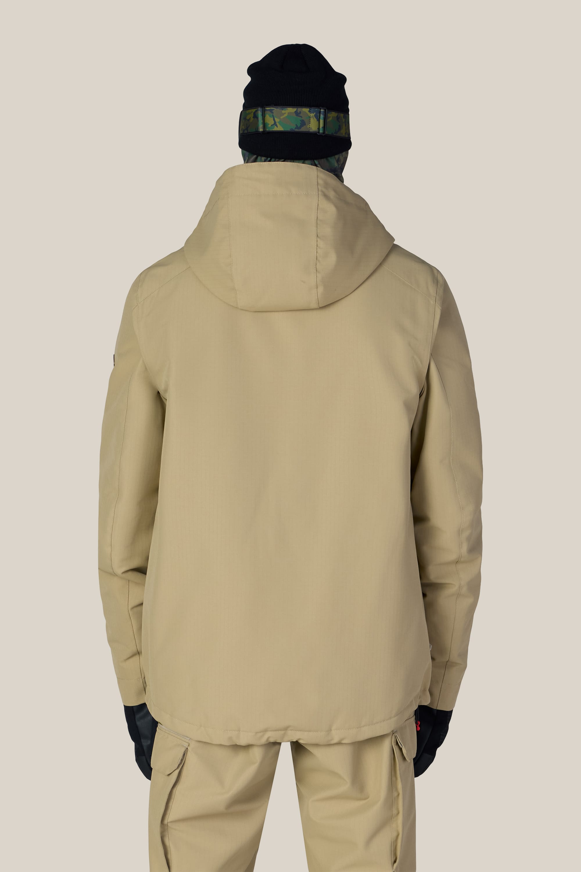 A person is shown from the back against a plain light background, wearing the 686 Men’s Nightline™ Insulated Jacket in tan with matching pants, paired with black gloves and a black beanie featuring a camouflage band.