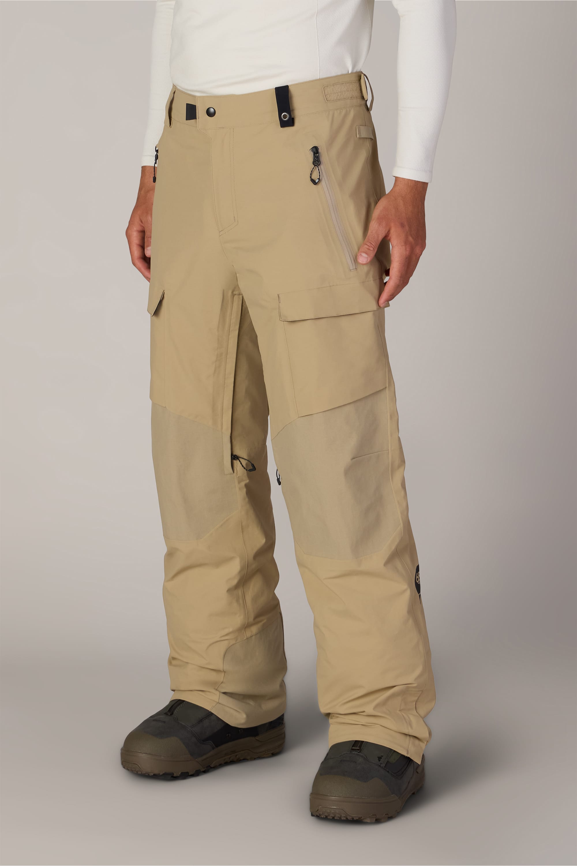 A person wearing 686 Men’s GORE-TEX® Dispatch™ Shell Pant in tan, paired with dark hiking boots, is shown from the shoulders down against a plain light background.