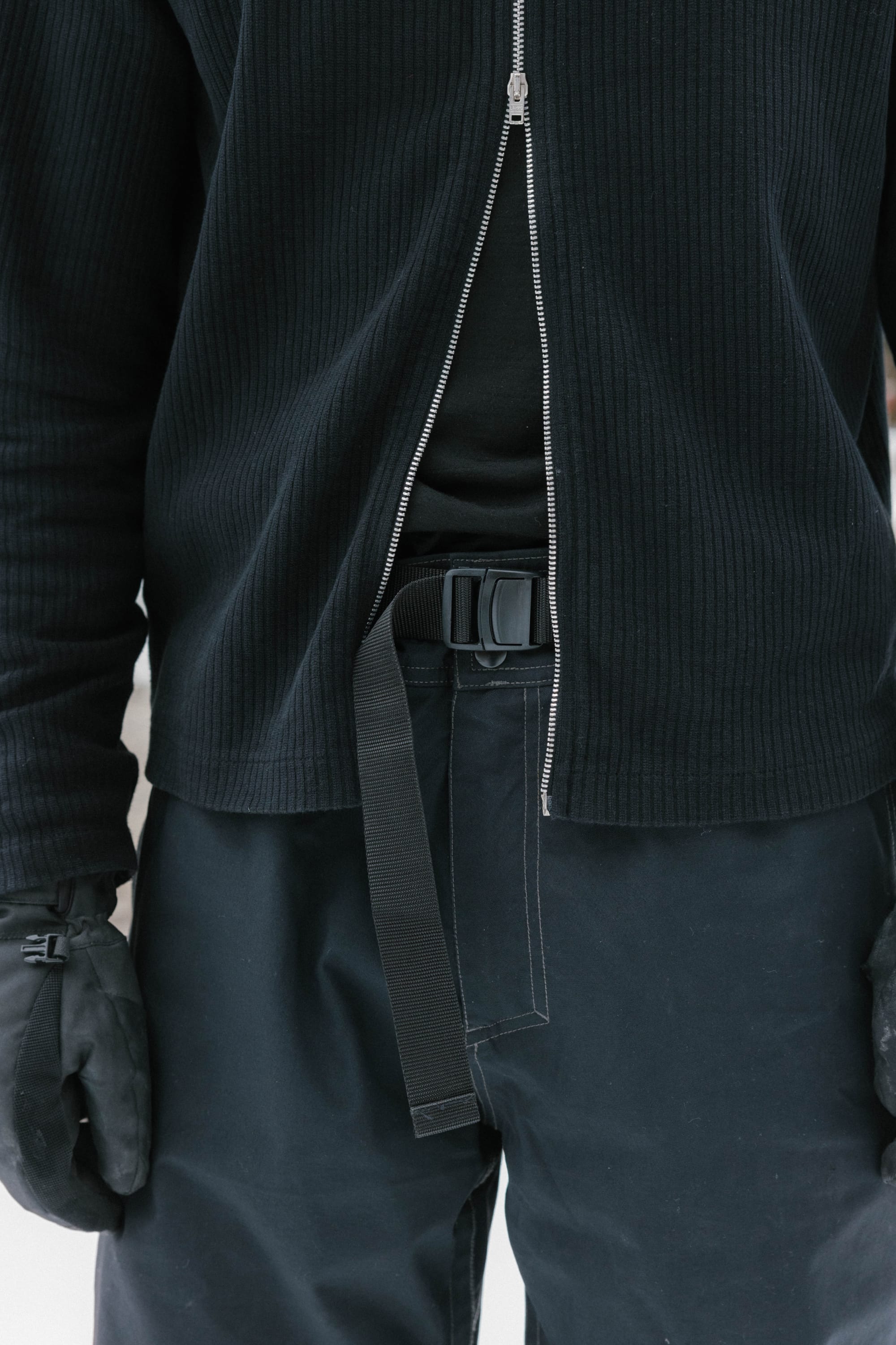 Someone wearing black gloves, a black shirt under a ribbed zip-up jacket, and 686 Dojo® Pant by 686 with a black belt. The photo is cropped between the chest and above the knees.