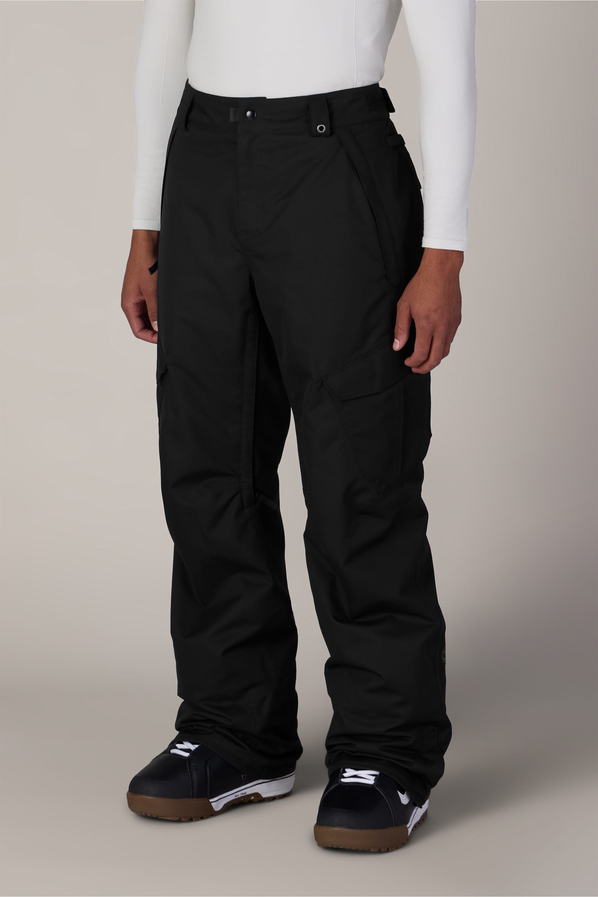 A person wearing a white long-sleeve shirt, the 686 Men’s Infinity™ Insulated Cargo Pant in black, and black snowboard boots stands against a plain background.