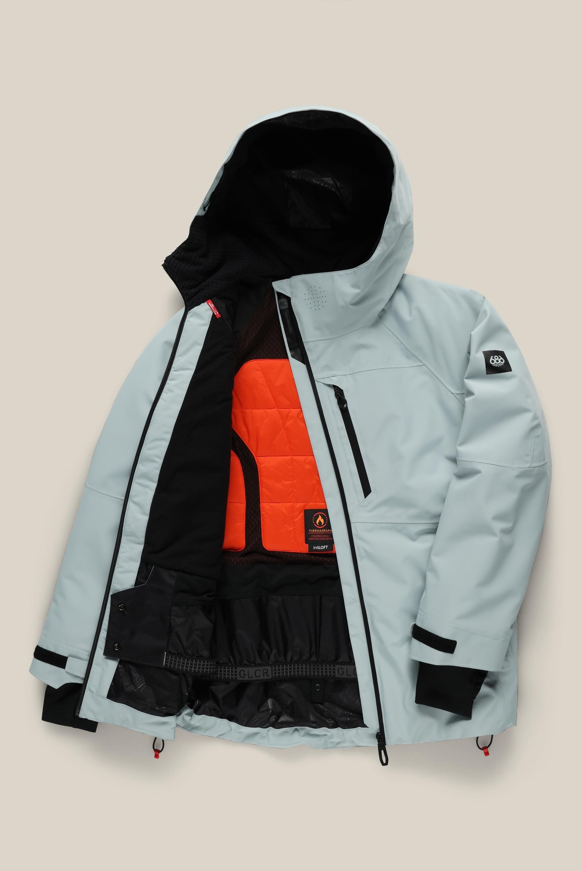 The 686 Women's Hydra™ Thermagraph® Jacket by 686 is shown open, featuring a light gray exterior, bright orange quilted lining, multiple pockets inside and out, black accents, and adjustable cuffs and hem.