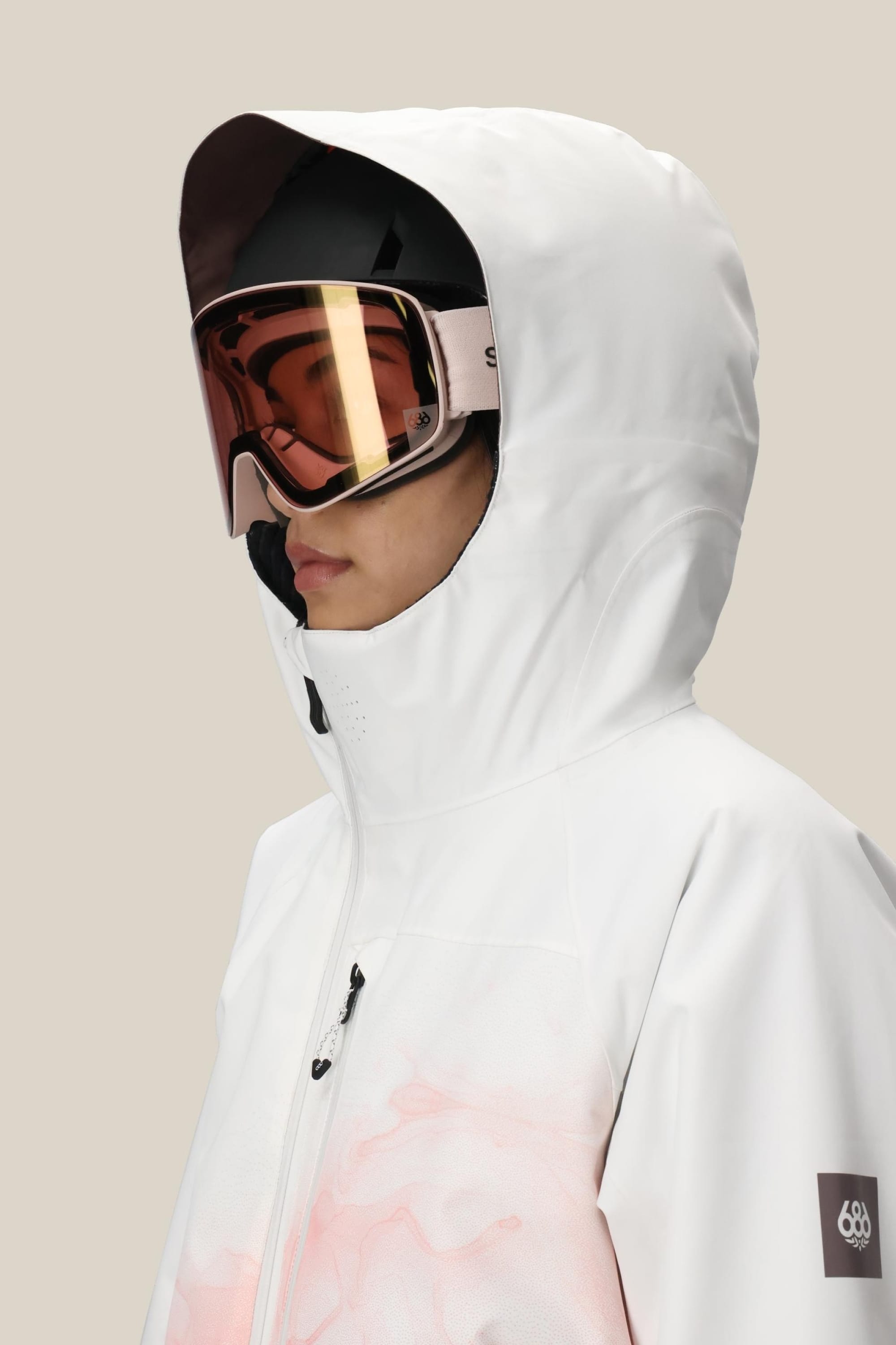A woman in the 686 Women's Hydra™ Thermagraph® Jacket, featuring a white hood, subtle pink pattern, and small sleeve logo, faces sideways. Reflective ski goggles and a light background highlight this stylish 686 waterproof jacket.