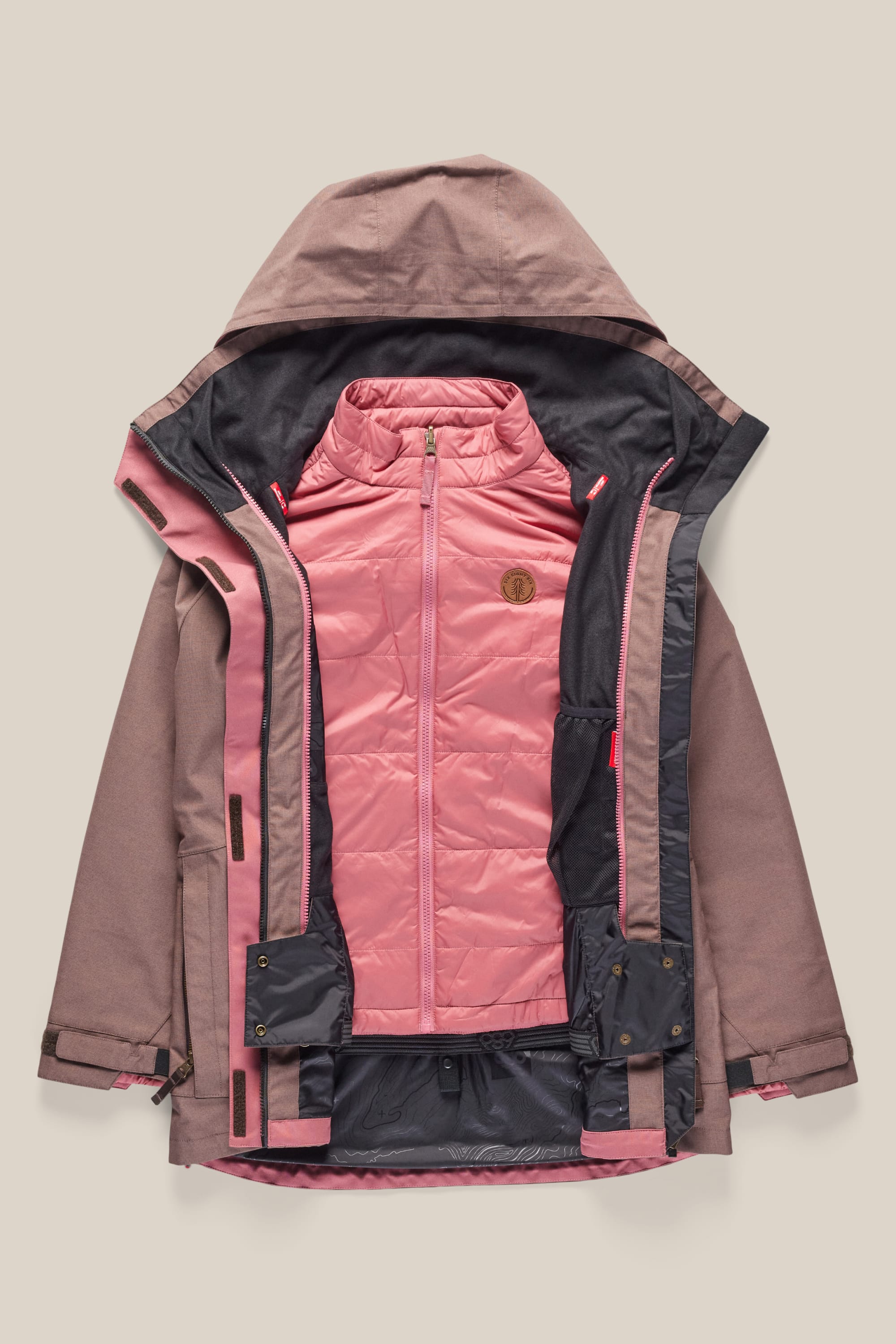 The 686 Women's SMARTY® 3-In-1 Spellbound Jacket by 686, in mauve polyester, is displayed unzipped on a beige background to reveal its quilted, removable pink inner layer with stand-up collar and brown circular chest logo. Waterproof design for winter wear.