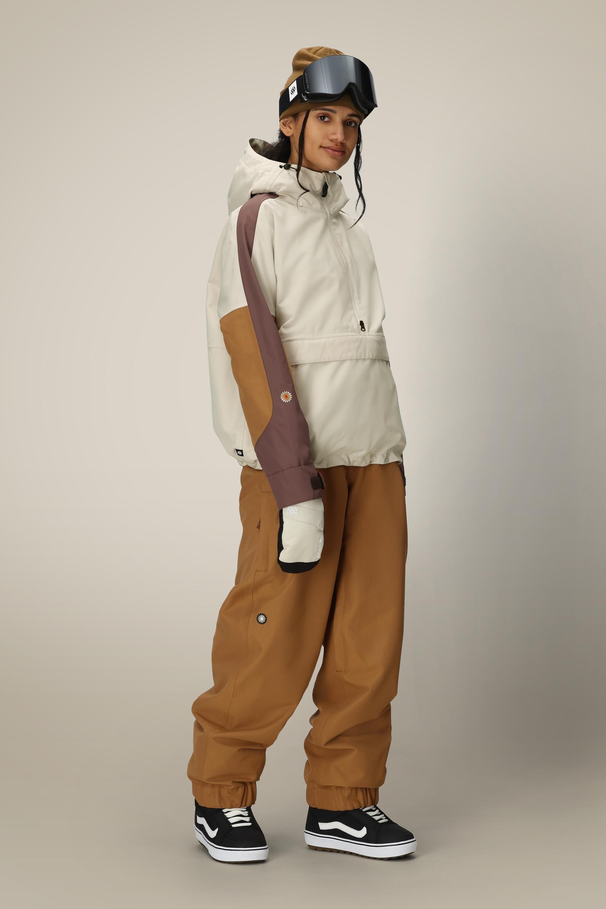A person wearing the 686 Women's Outline™ Shell Anorak, matching pants, ski gloves, goggles on their head, and black Vans sneakers stands against a plain light background.