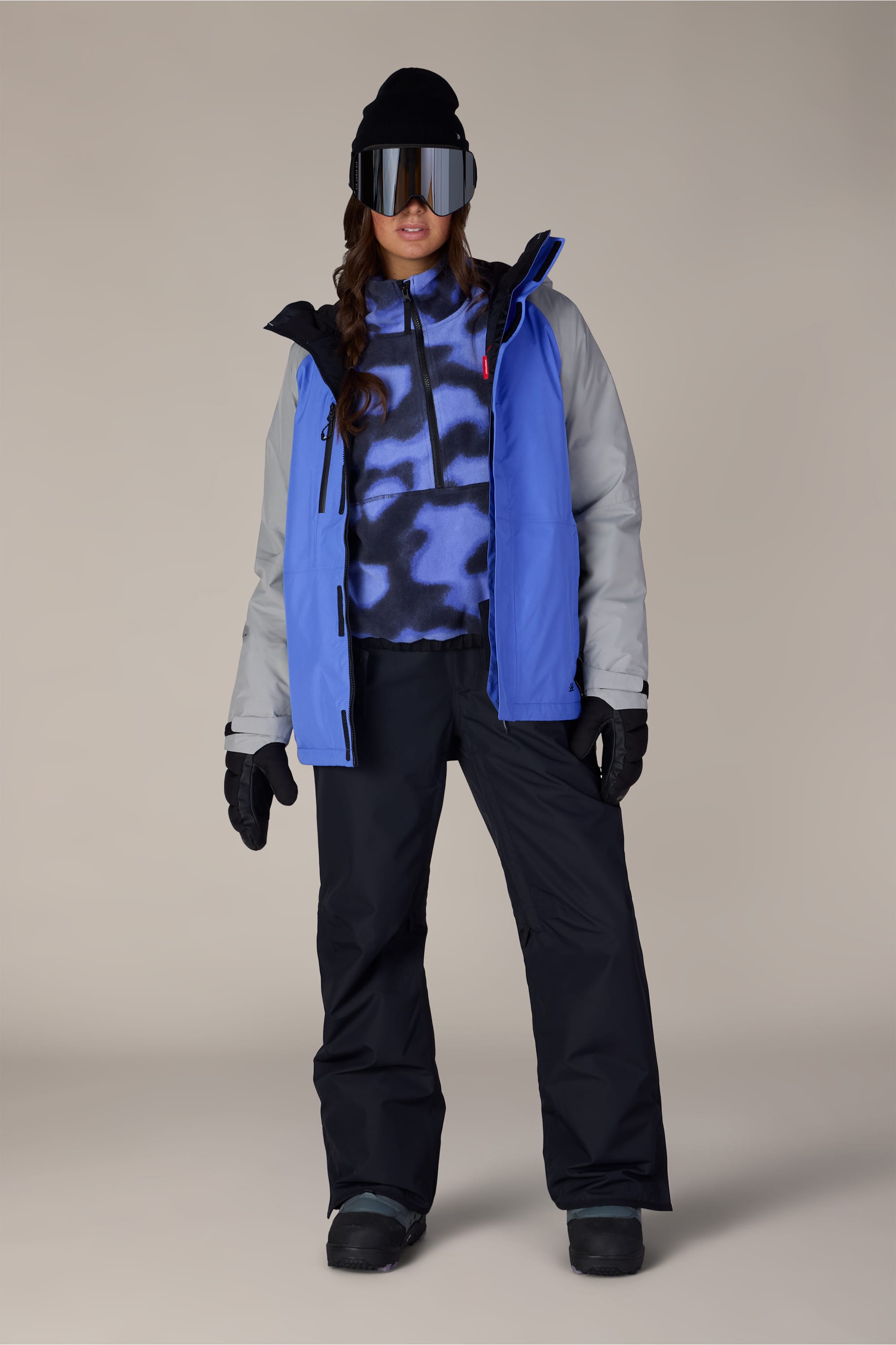 A person wearing the 686 Women’s GORE-TEX® Willow™ Insulated Jacket stands facing forward against a plain background, styled with black snow pants, black gloves, a black beanie, and large ski goggles.