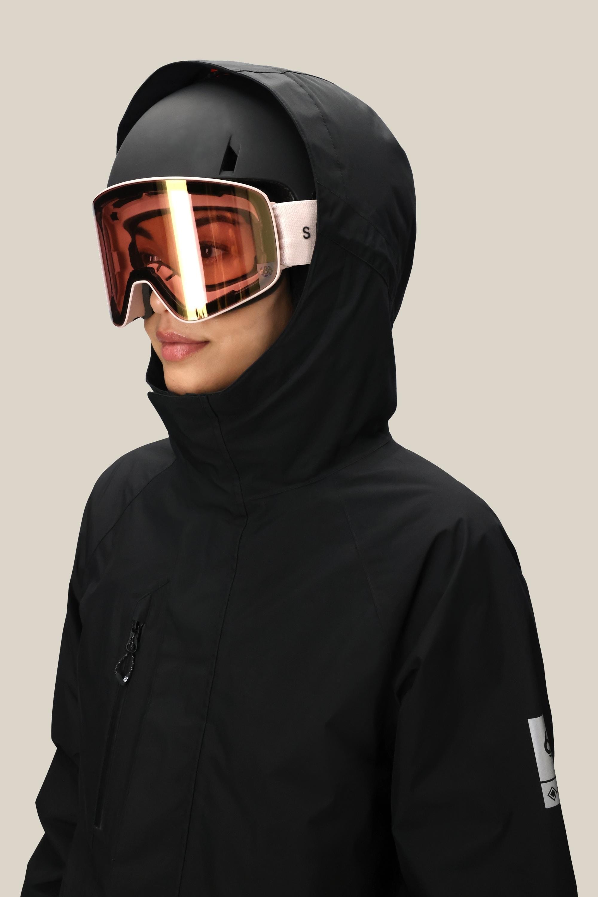 A person in the 686 Women's GORE-TEX Willow™ Insulated Jacket, black helmet, and reflective ski goggles looks to the side against a plain light background.