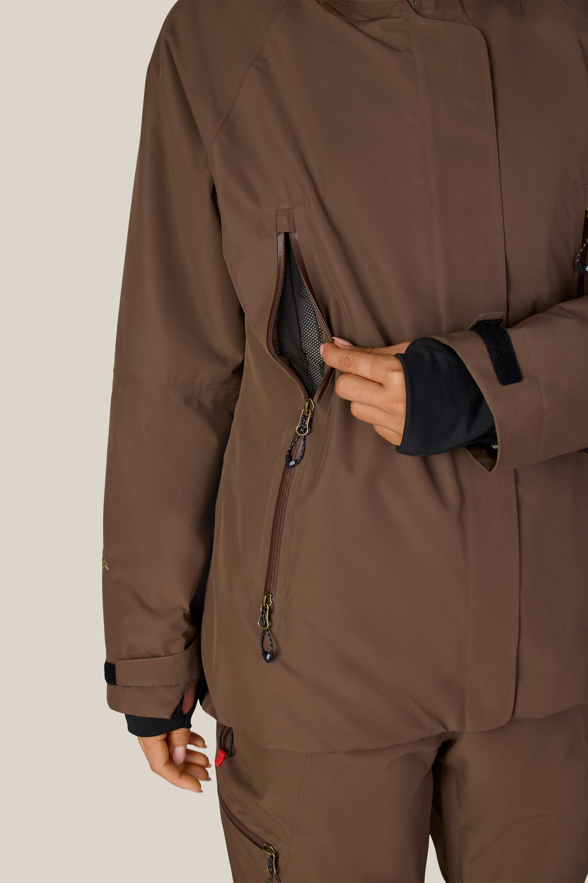 A person wearing the 686 Women’s Whisper™ Insulated Jacket unzips a mesh-lined chest pocket; only the torso and one hand are visible against a plain, light background.