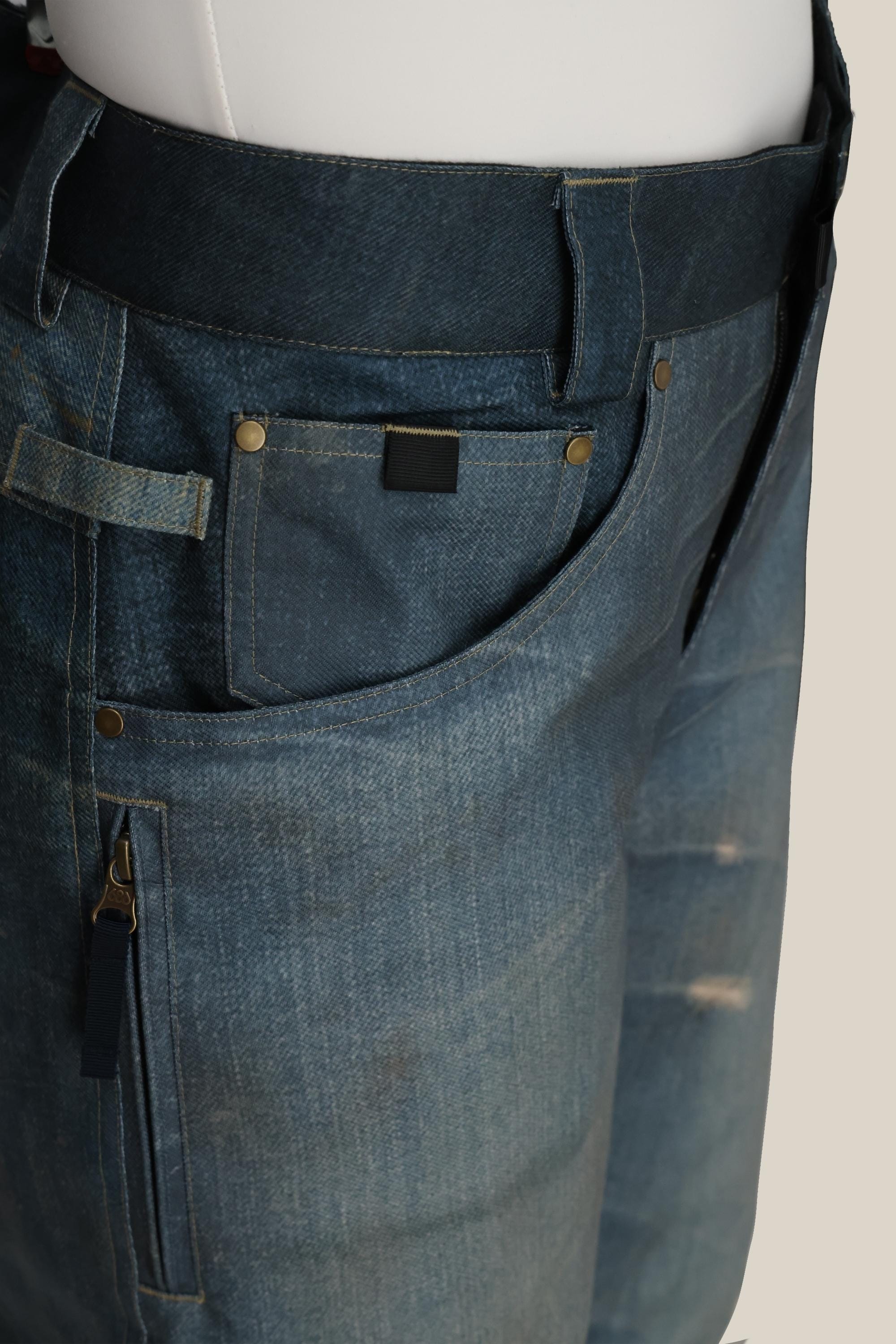 Close-up of the 686 Women's Deconstructedª Denim Insulated Pant by 686, featuring front pockets, belt loops, brass rivets, and zipper details. The denim has a slightly worn texture and faded areas for a stylish, lived-in look.