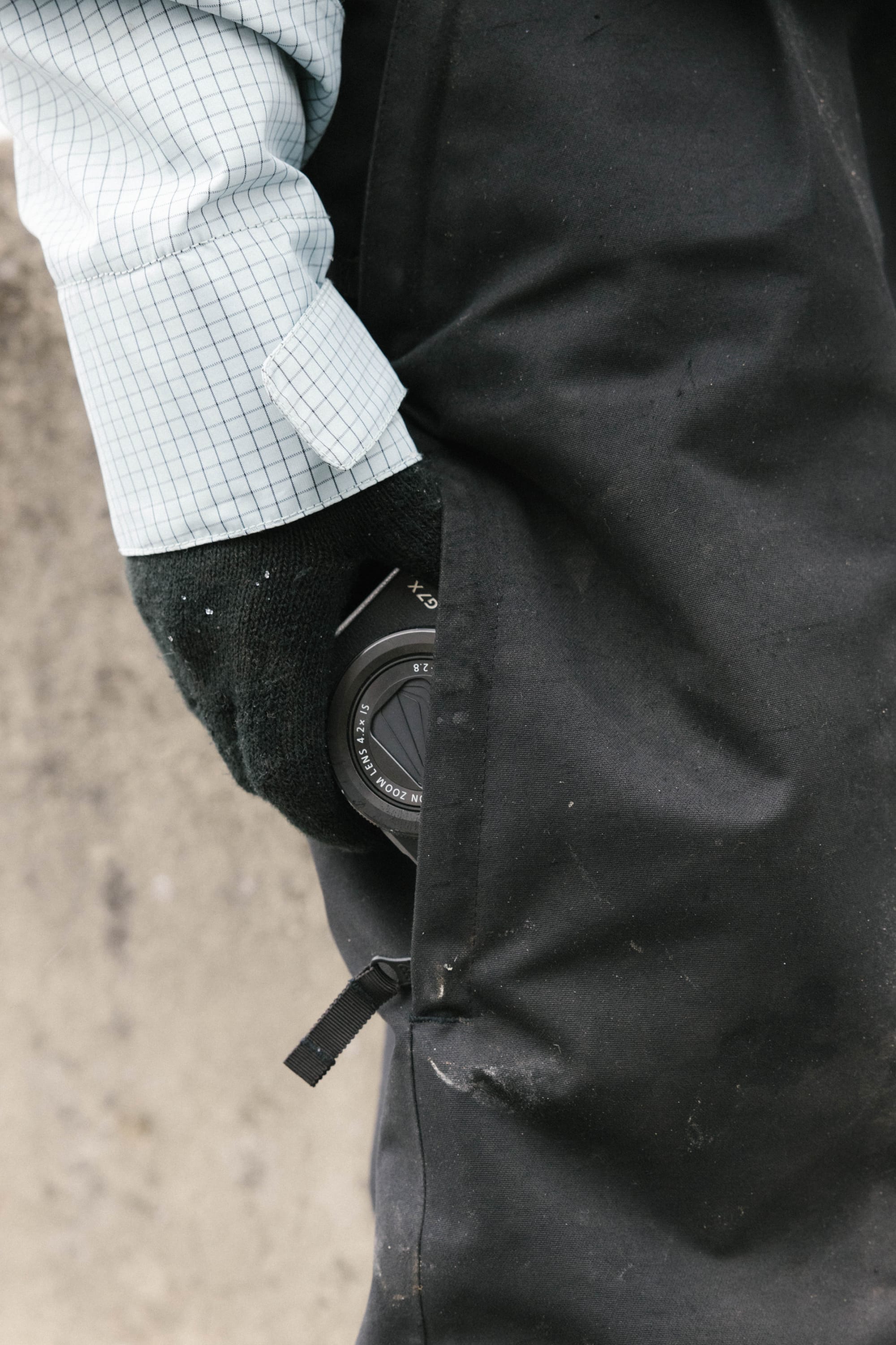 A person wearing a light blue checkered shirt and black gloves has a camera lens tucked into the pocket of stylish 686 Women's Outline™ Shell Pants.