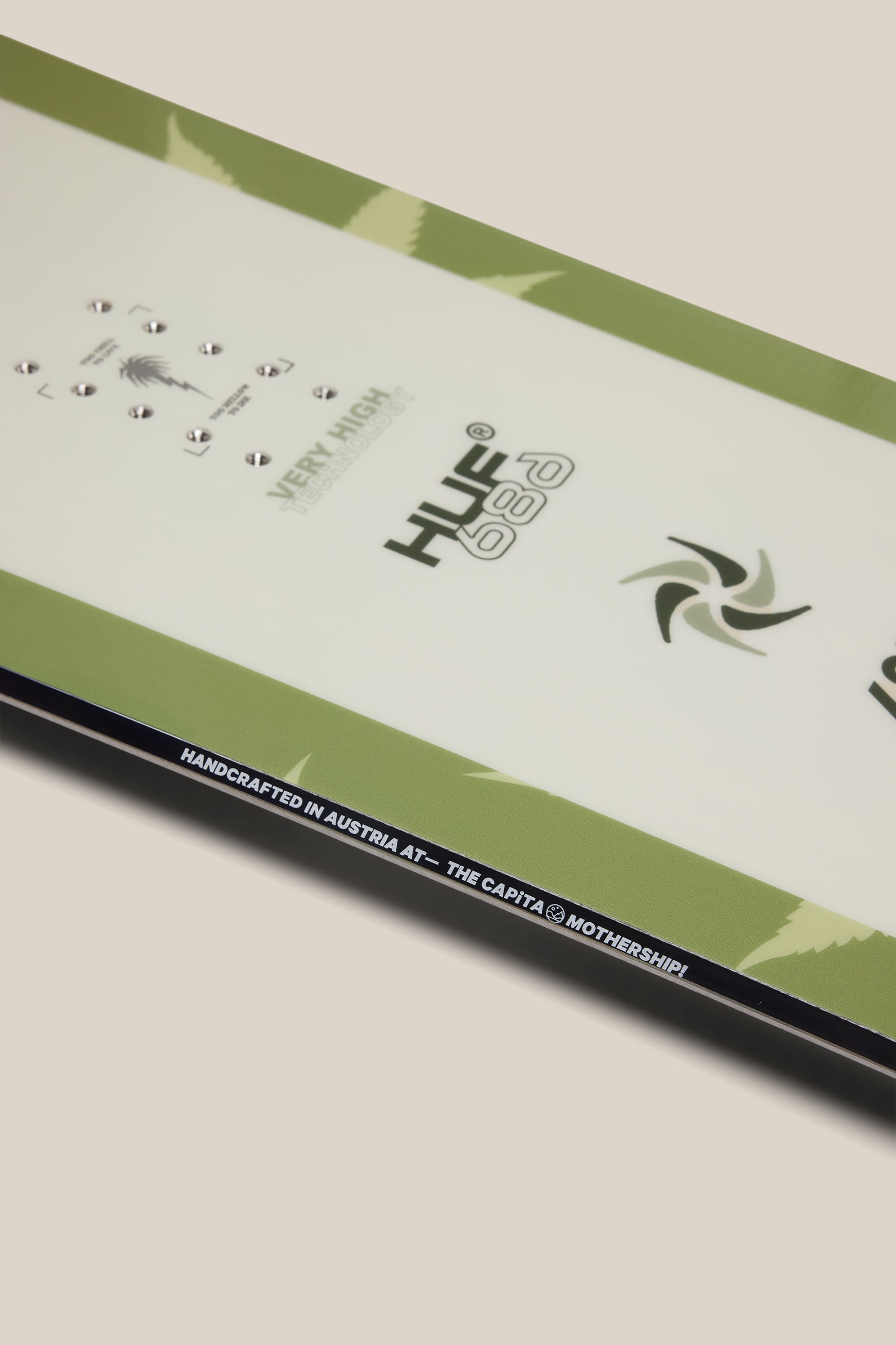 Close-up of the 686 HUF SB Slush Slasher Snowboard in green and white, featuring 686 and HUF logos. Text along the edge reads: HANDCRAFTED IN AUSTRIA AT—THE CAPITA MOTHERSHIP.