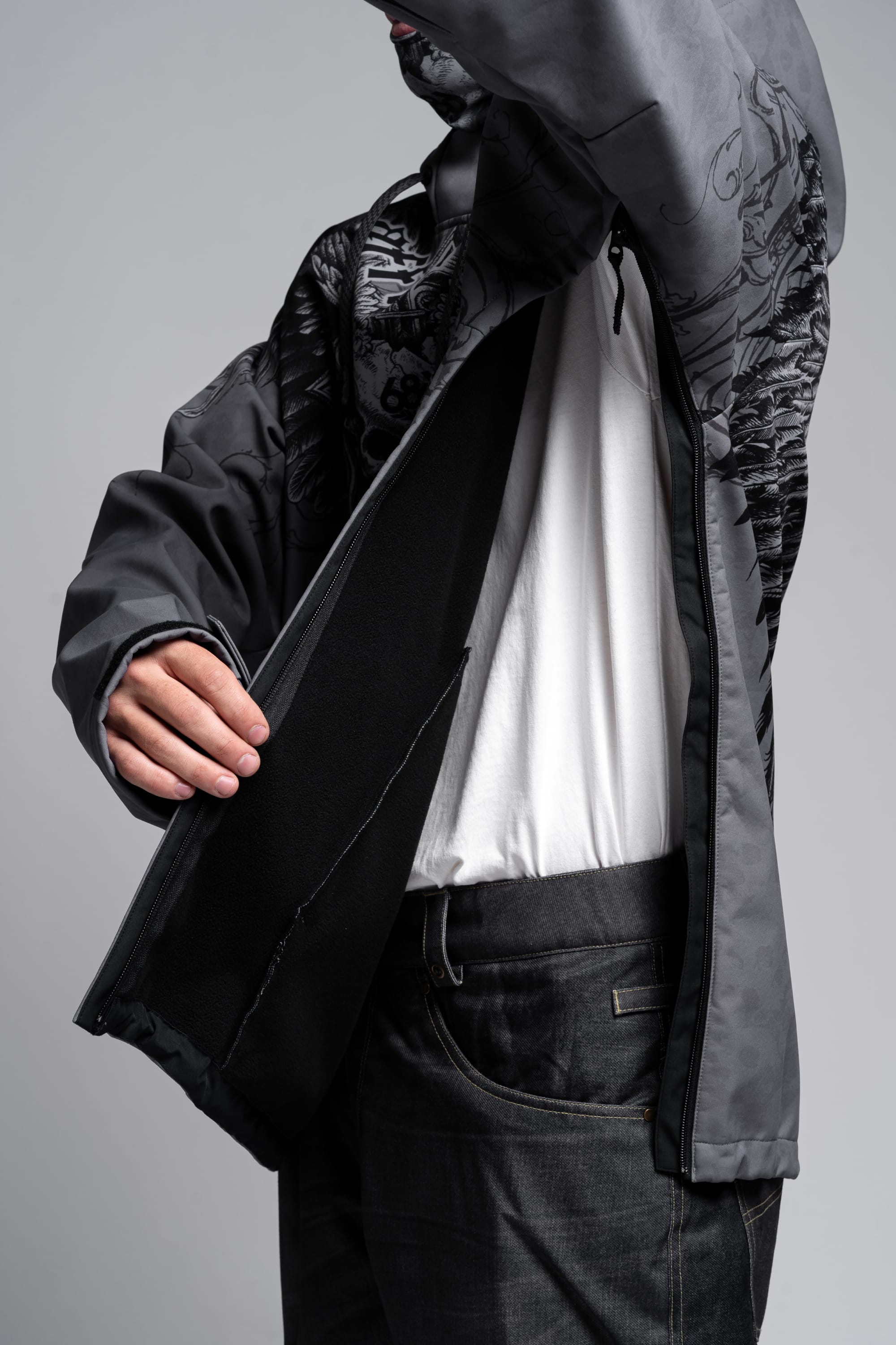 A person wearing the 686 Affliction Waterproof Hoody and dark jeans lifts their arm to show the large inner pocket of the unzipped jacket, facing sideways with their head partially out of frame.