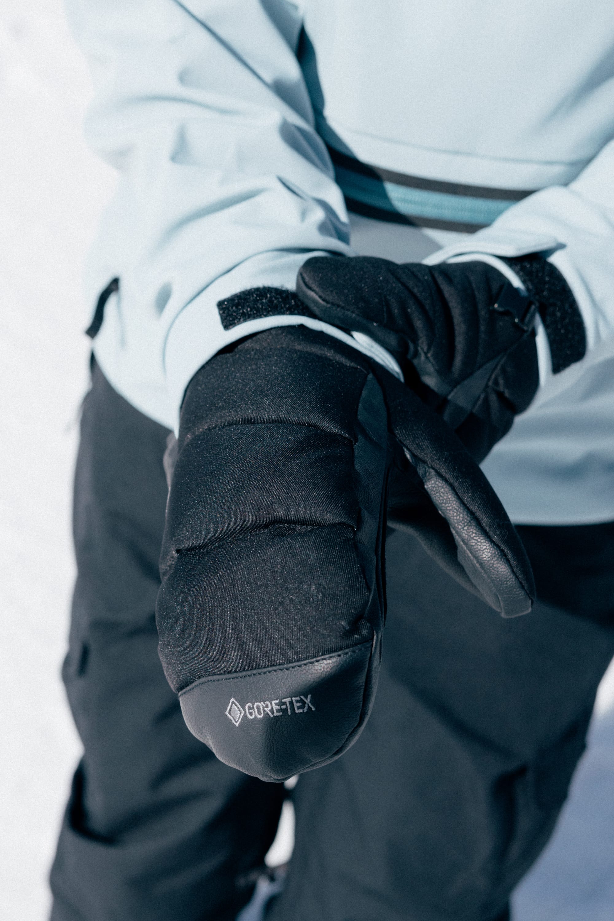 Wearing a light blue 686 Women’s Waterproof Hoody, a person stands on snow and holds out one mittened hand toward the camera.