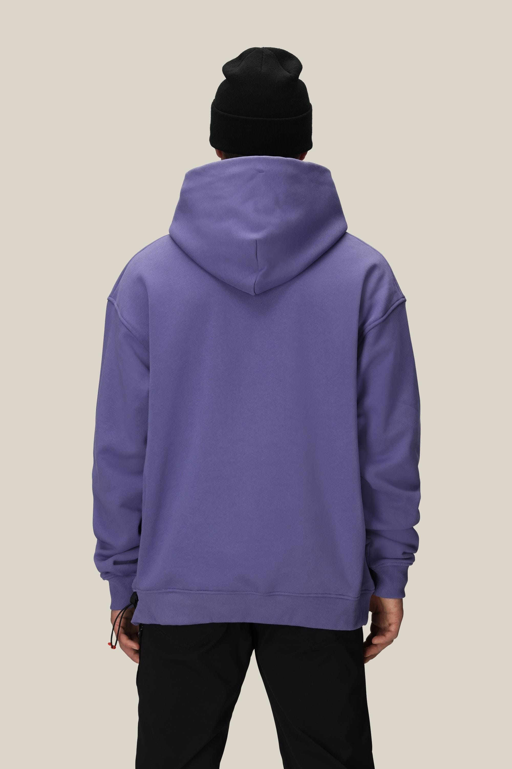 A person faces away from the camera against a plain beige background, wearing a black beanie, black pants, and the 686 Knockout Logo Premium Heavyweight Pullover Hoody by 686 in purple.