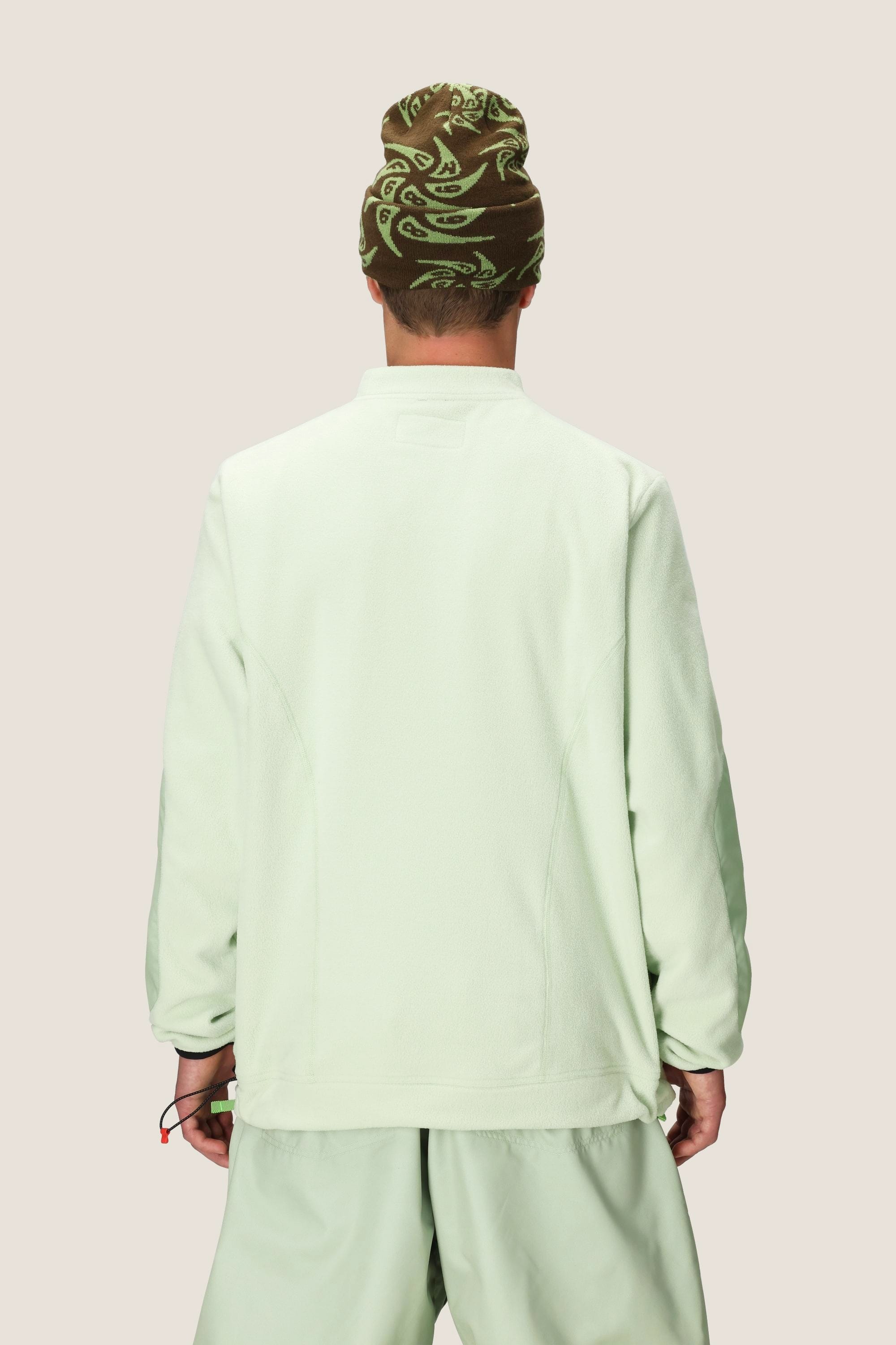 A person stands facing away, wearing the 686 Mens HUF Fleece Crewneck in light green by 686 with matching pants and a brown beanie with a light green swirl pattern, set against a plain light background.