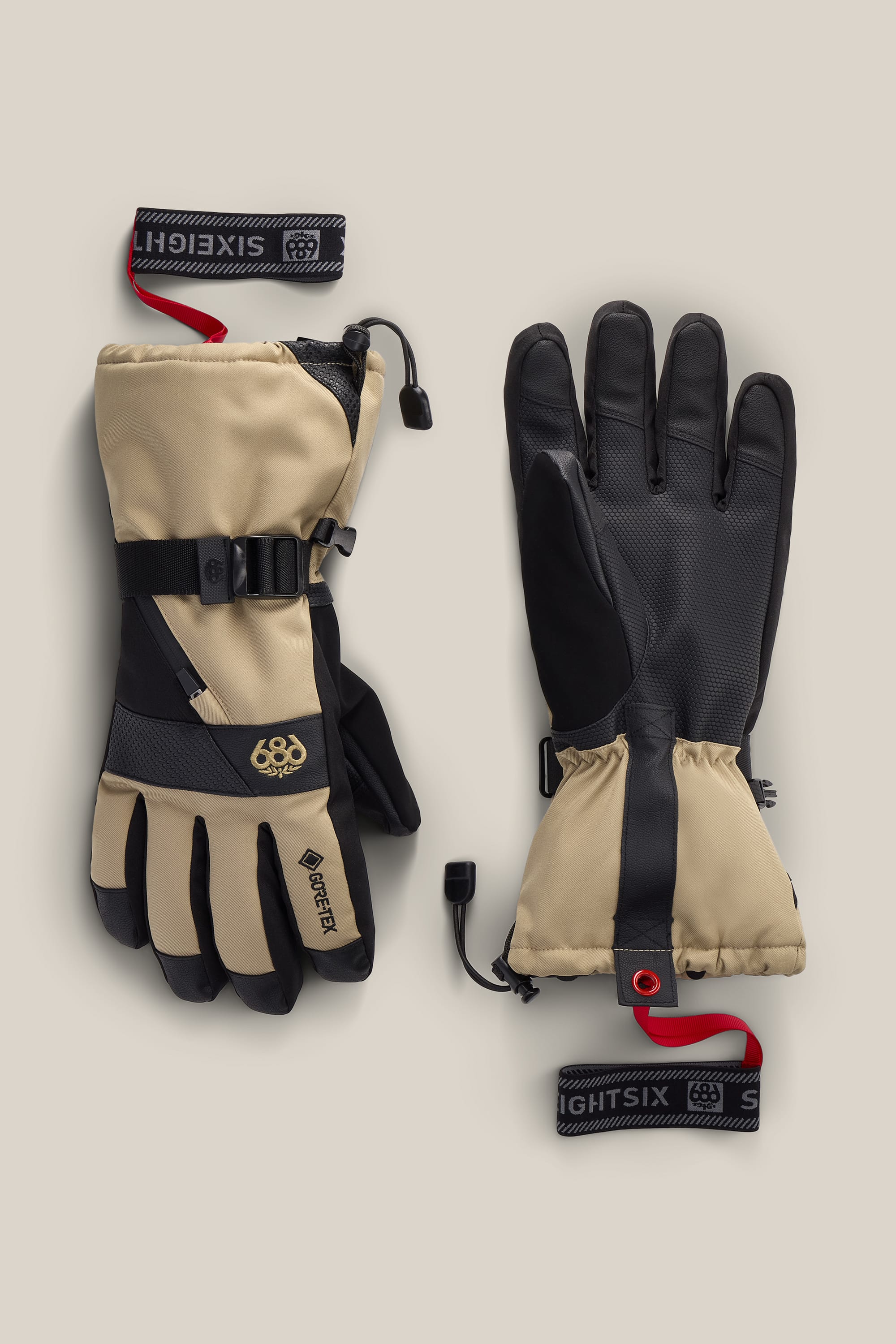 A pair of 686 Men’s GORE-TEX® SMARTY® 3-In-1 Gauntlet Gloves in tan and black, featuring adjustable straps and red wrist leashes, is displayed palm up and palm down on a neutral background.