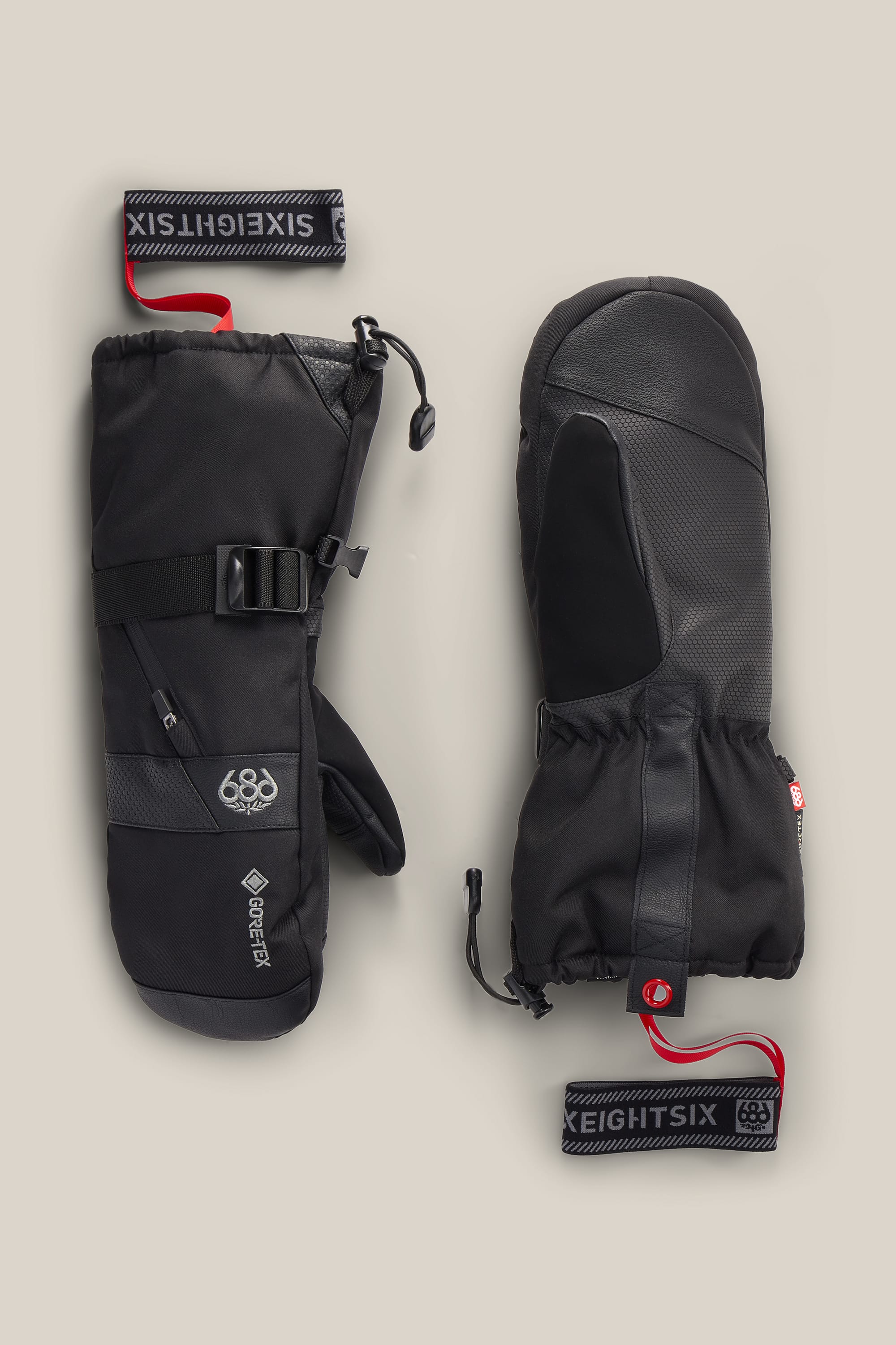 Two black 686 Men’s GORE-TEX® SMARTY® 3-In-1 Gauntlet Mitts featuring adjustable straps, textured grip palms, and red 686 tags attached to the wrists, displayed on a neutral background.