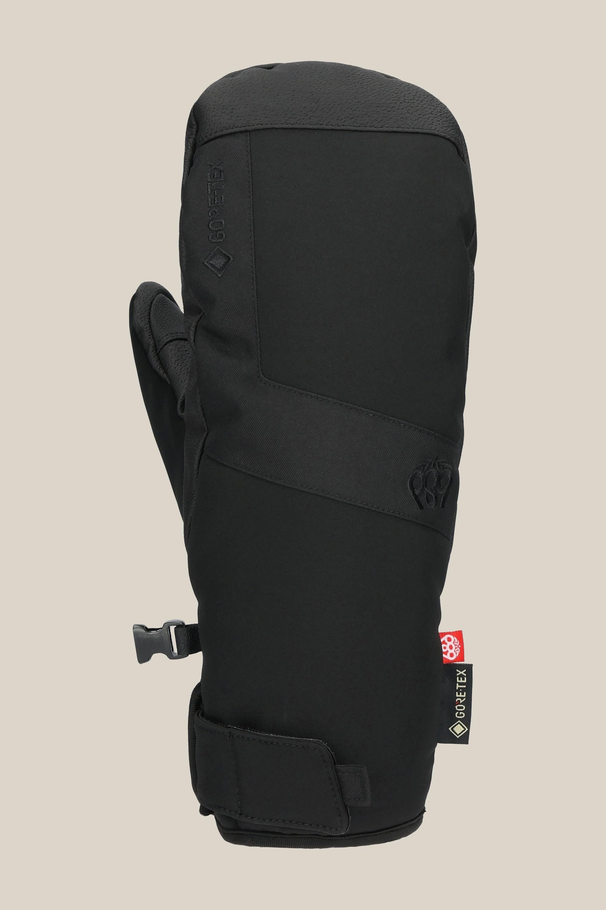The 686 Men's GORE-TEX Linear™ Under Cuff Mitt is a black insulated mitt with strap and Velcro closure, GORE-TEX tag, and small geometric logo on the back, shown against a plain beige background.