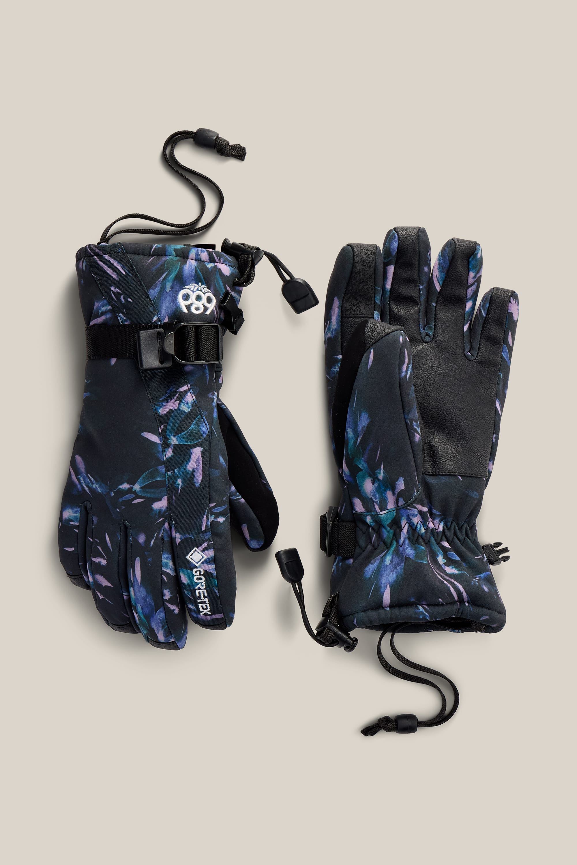 The 686 Women’s GORE-TEX® Linear™ Gloves by 686, featuring a dark floral pattern, adjustable wrist straps, and drawstring cords, are displayed on a neutral background.