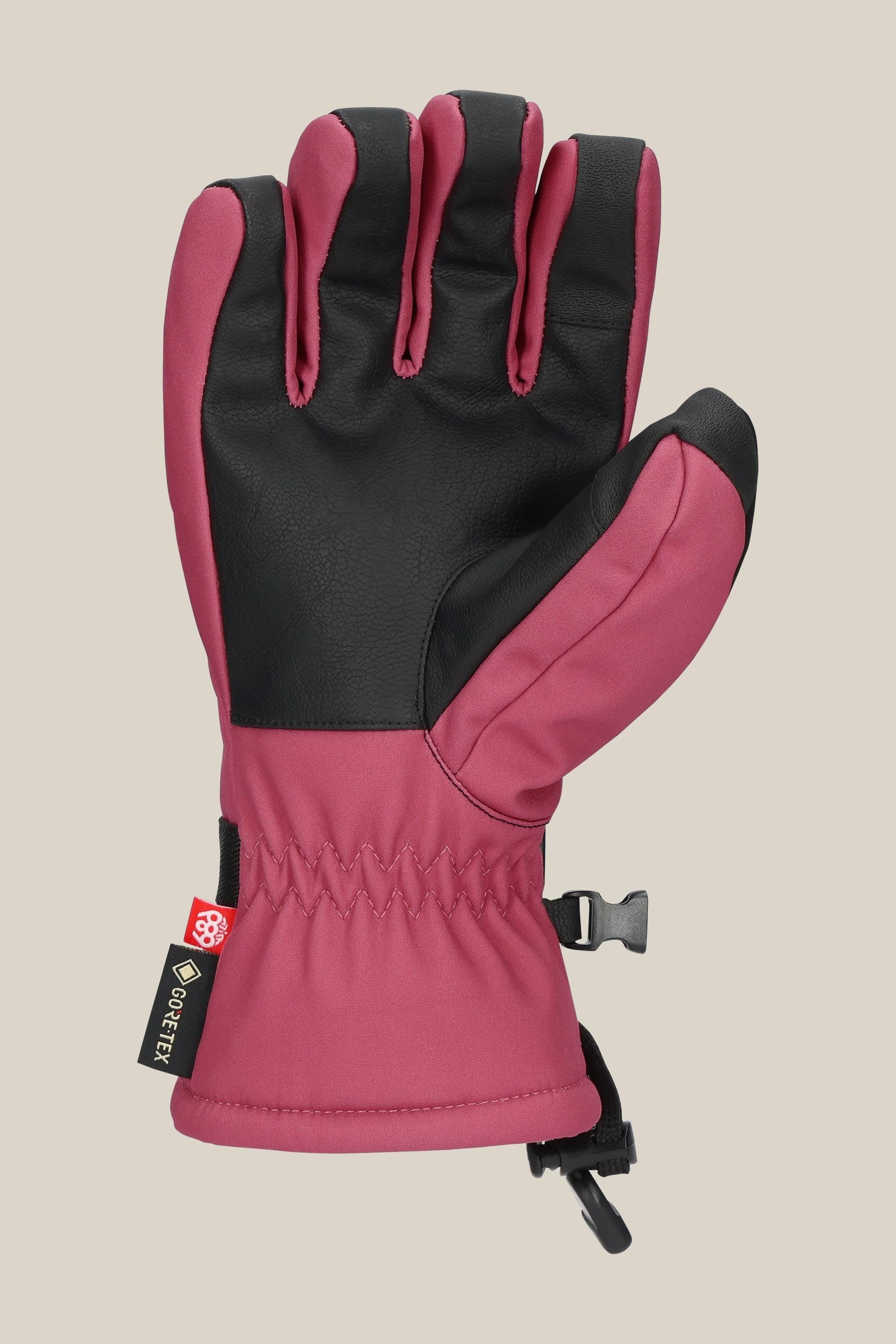 The 686 Women's GORE-TEX Linear™ Glove by 686 features a pink and black design with a black palm and thumb, adjustable wrist strap, GORE-TEX tag, and is shown on a light beige background.