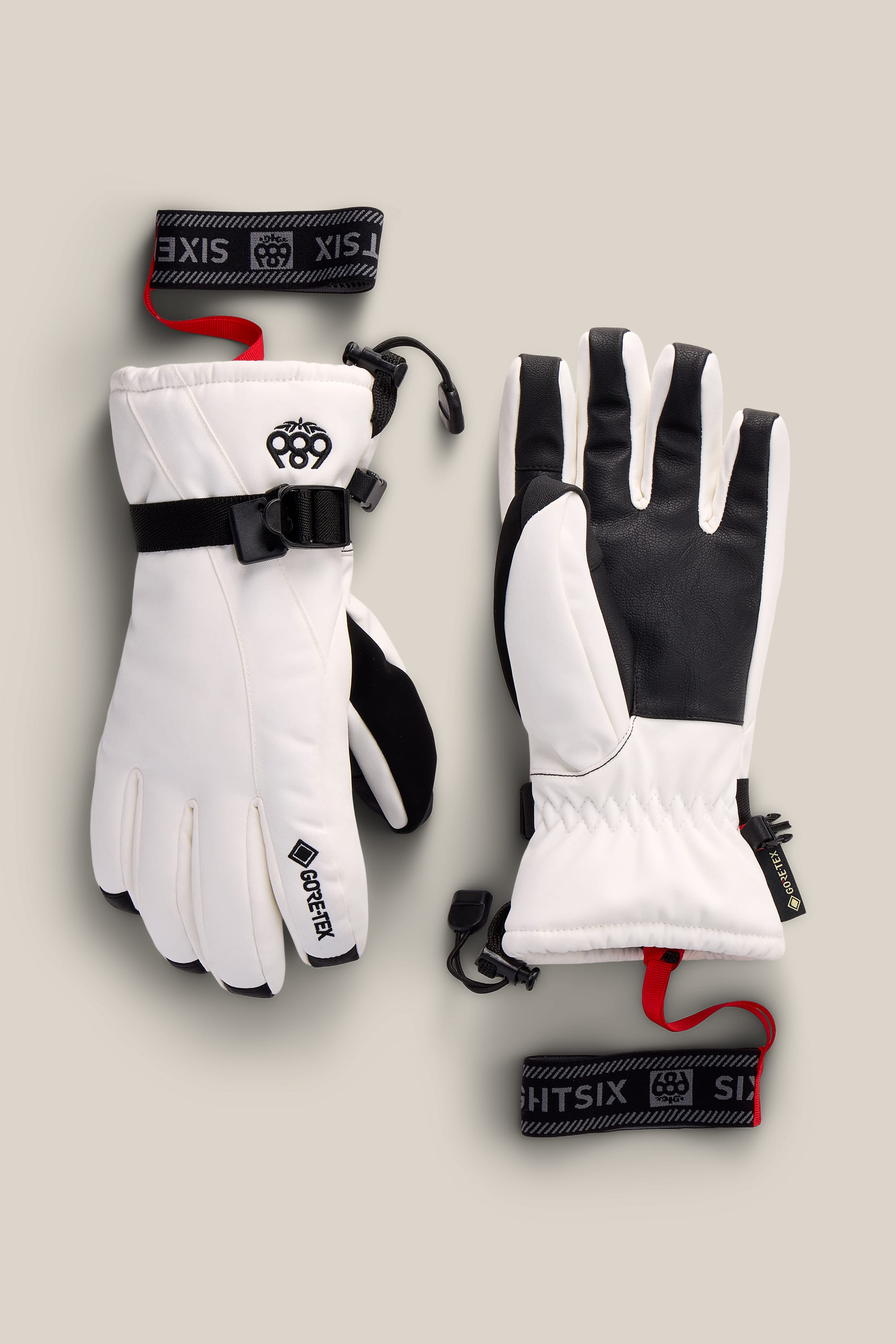 The 686 Women’s GORE-TEX® Linear™ Gloves by 686, featuring a white and black design with adjustable wrist straps, black palms, and GORE-TEX® tags, are laid flat on a neutral background.